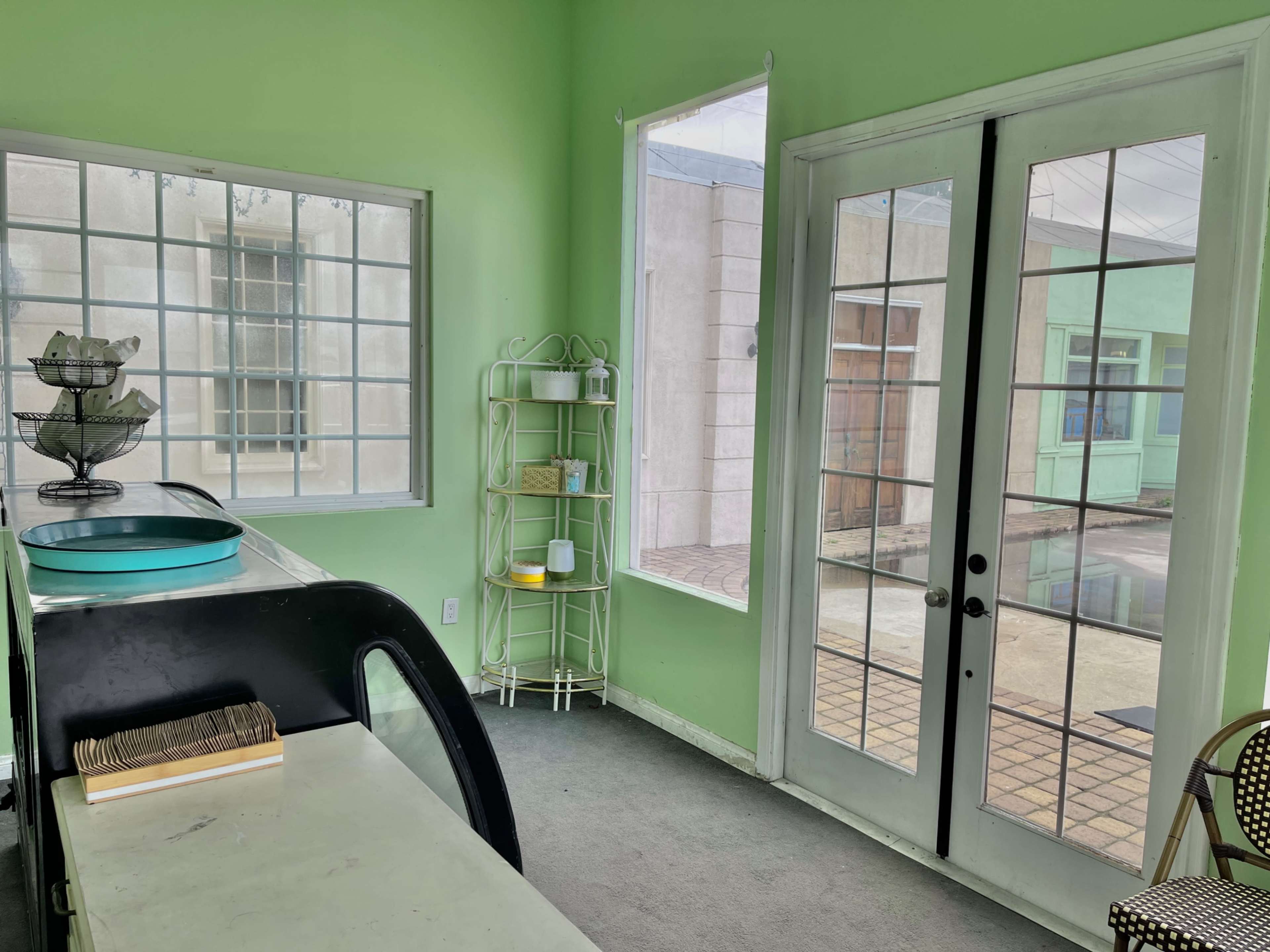The image shows a green-walled room with large windows, double glass doors, and a white shelf containing various items.