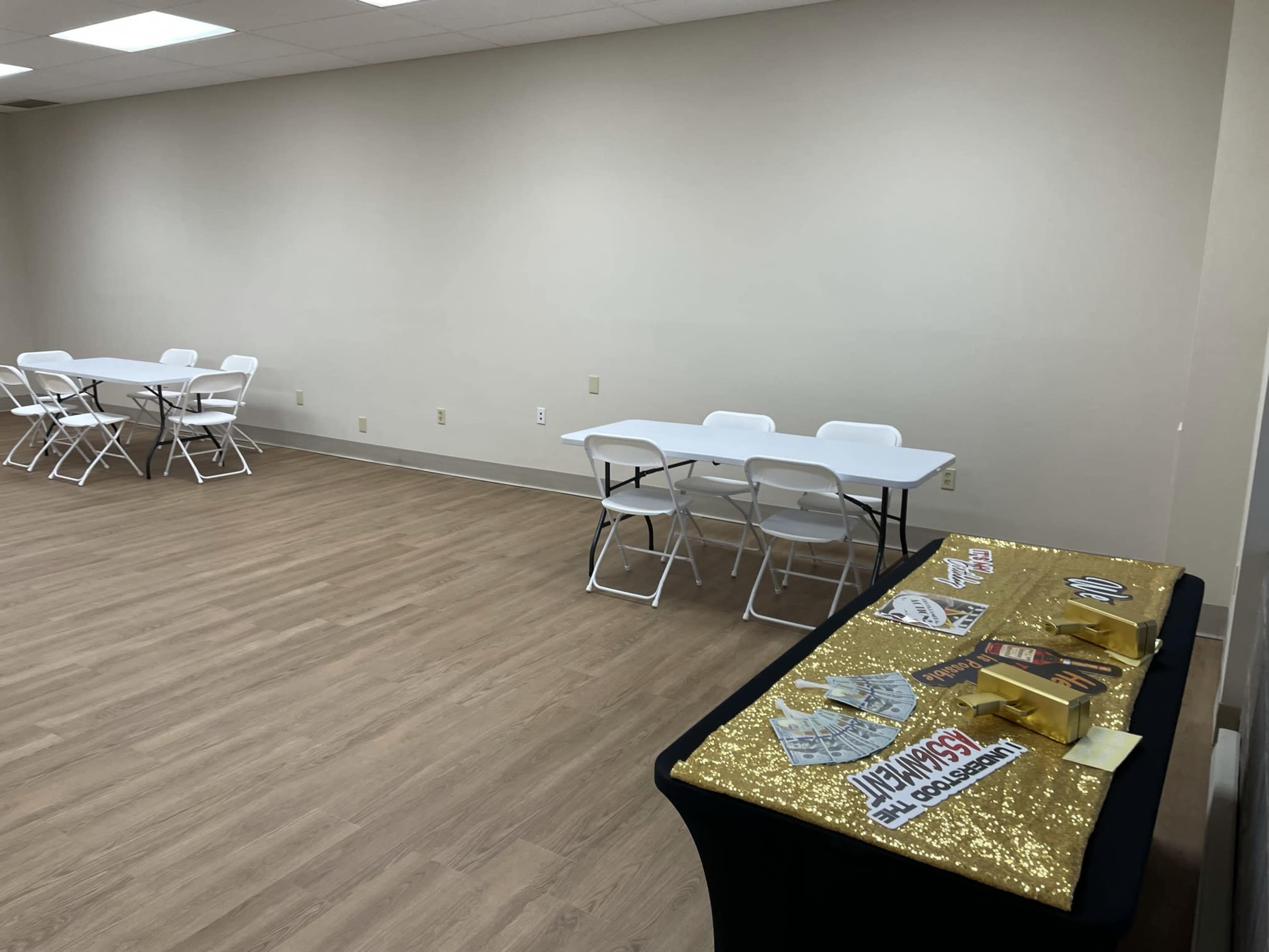 A spacious room features several folding tables and a decorated table with gold accents and promotional materials.