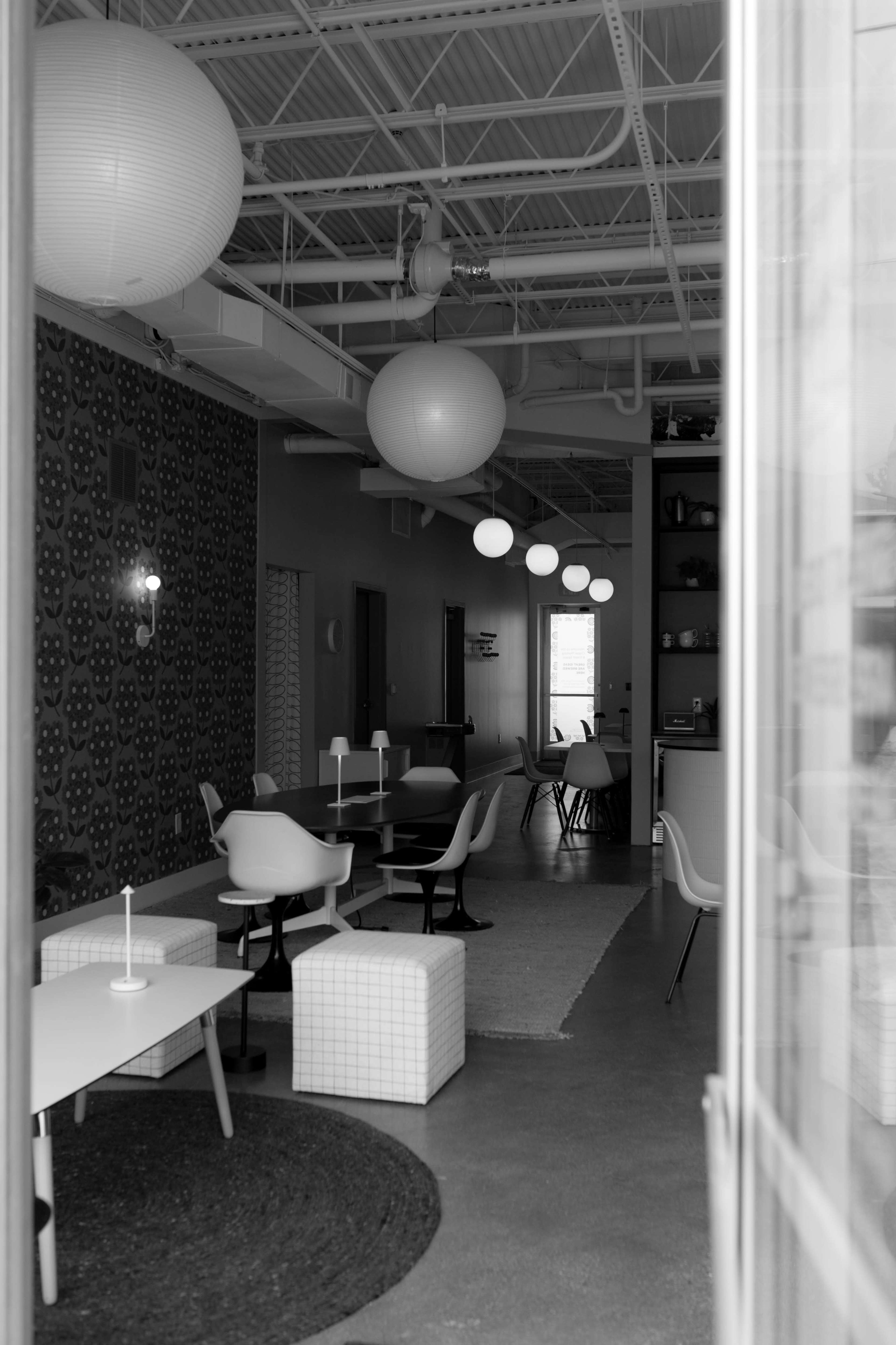 The image shows a modern interior space with multiple seating areas, large light fixtures, and a patterned accent wall.