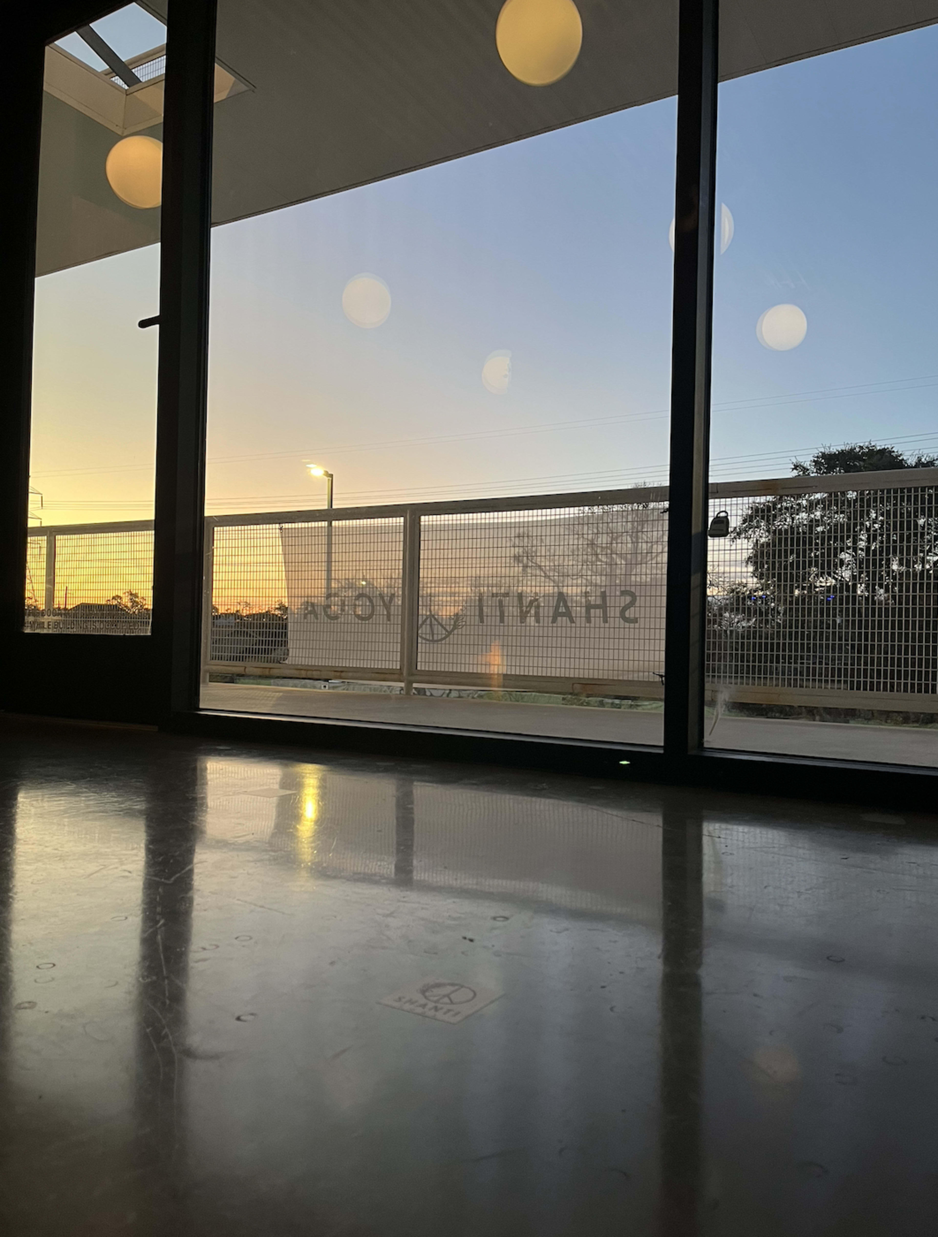 The image shows a glass door with a sign that reads "SHANTI YOGA," framed by a sunset outside and a polished floor inside.