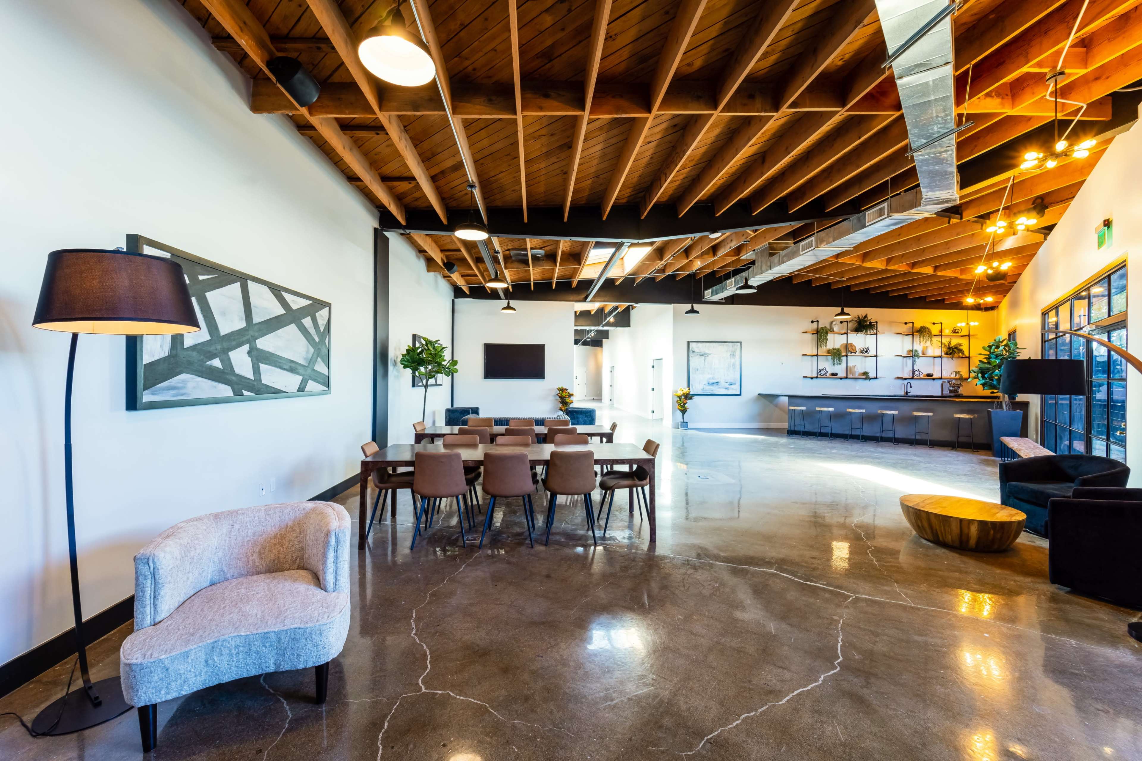 The image shows a modern interior space featuring a dining table with chairs, a lounge area, and a reception counter, all beneath a wooden ceiling.