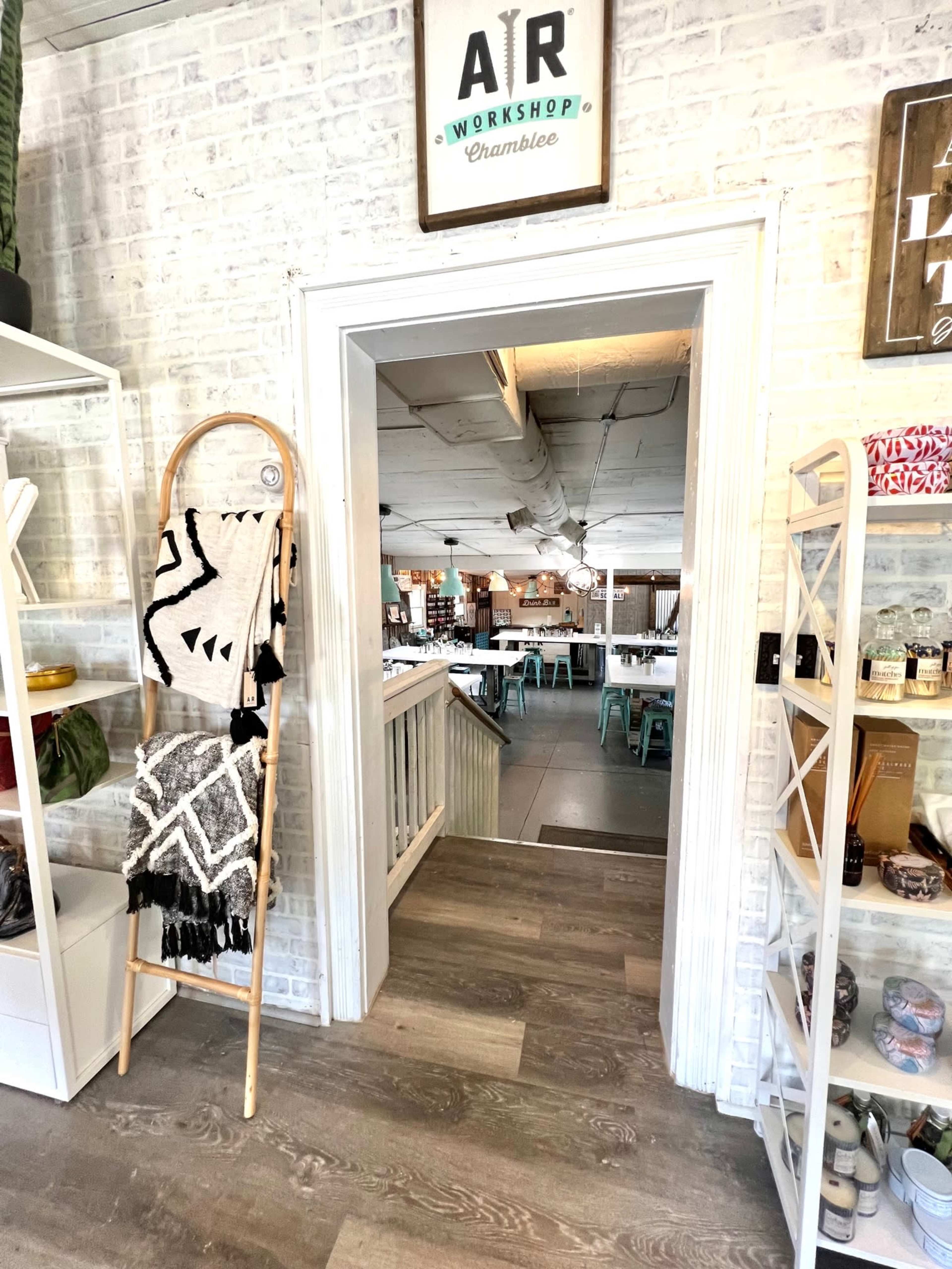 A wooden ladder display holds a patterned blanket beside an open doorway leading into a brightly lit workshop space with tables and chairs.