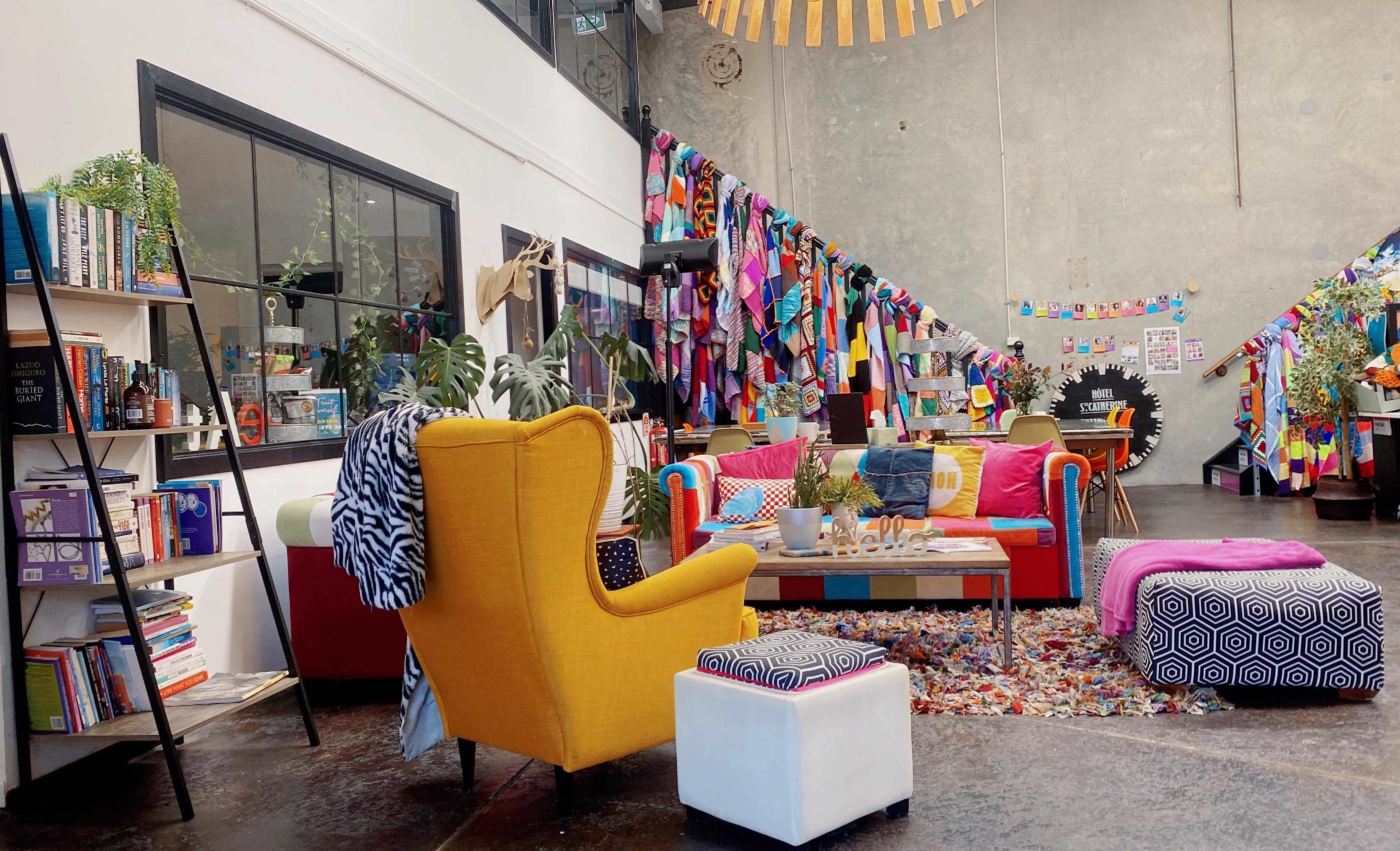 A vibrant communal space featuring colorful furniture, a bookshelf, and a wall decorated with fabric banners.