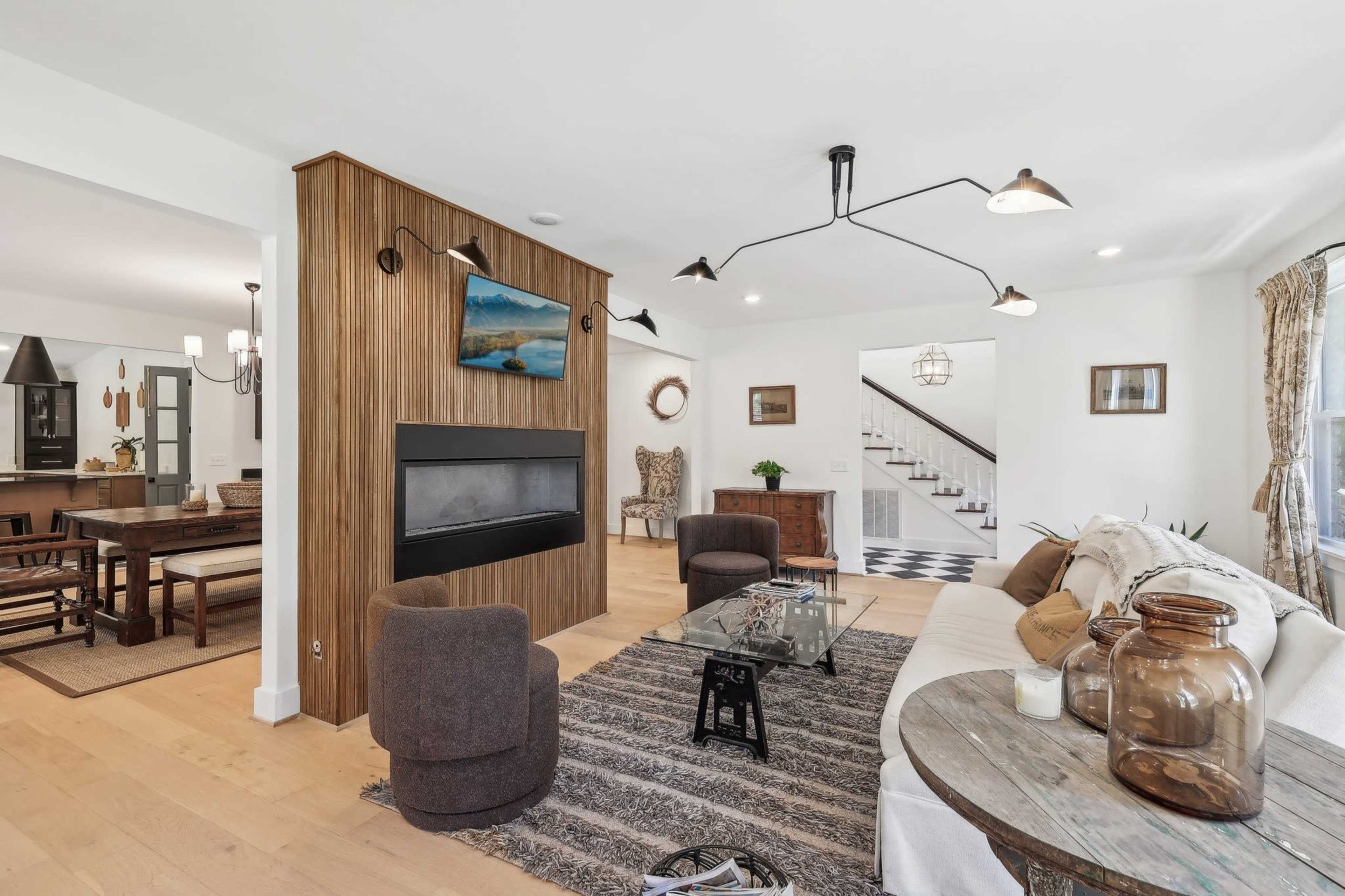 A modern living room with a fireplace, a glass coffee table, and a dining area in the background.