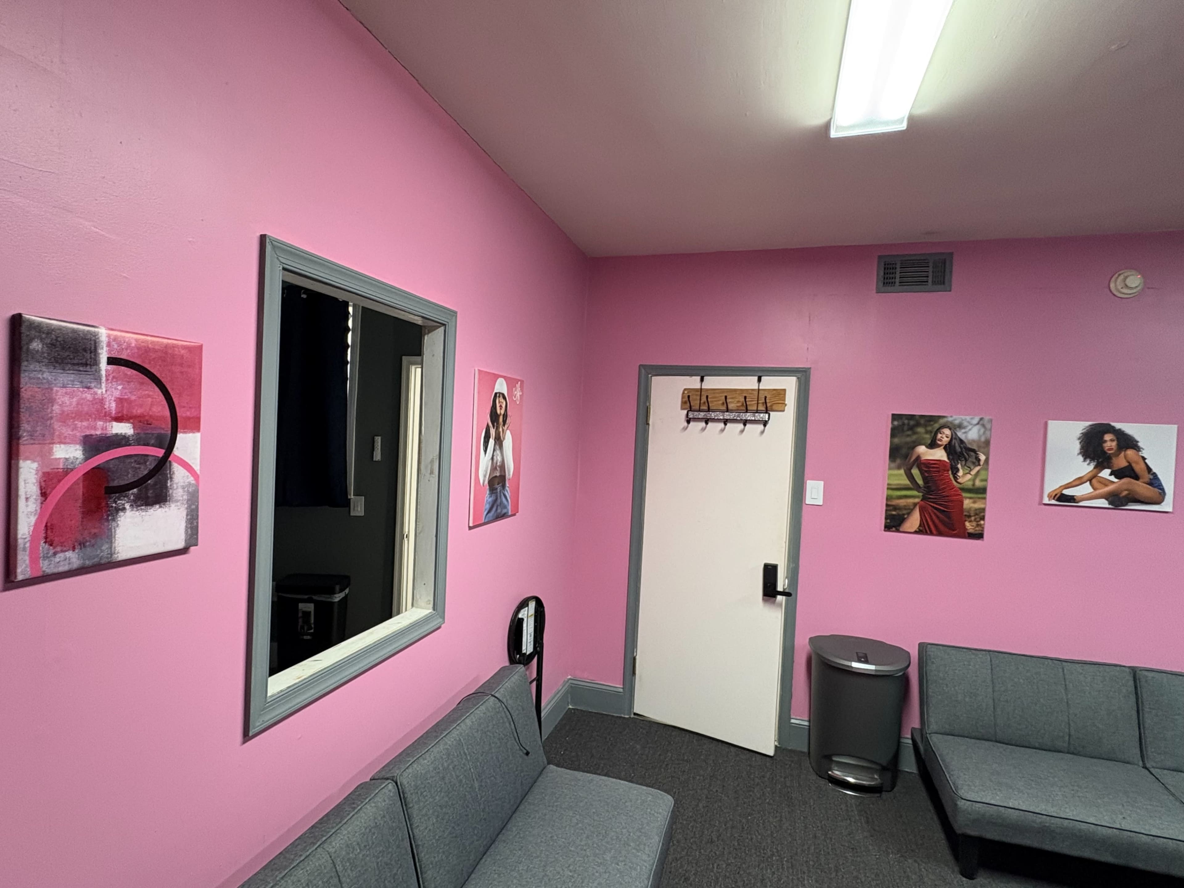 The image shows a pink-walled room with two gray sofas, a waste bin, and framed artwork on the walls.