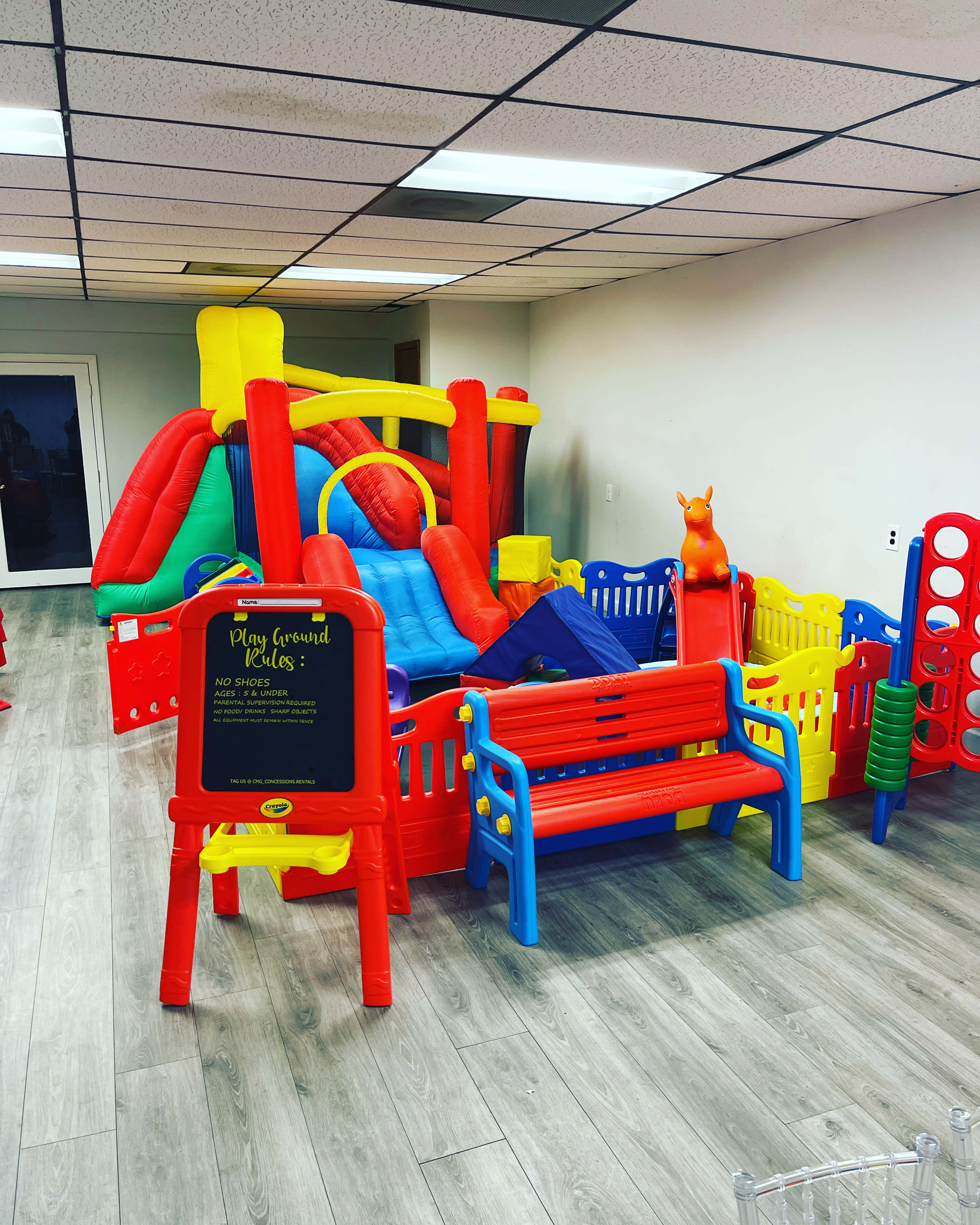 A colorful indoor playground filled with various plastic play structures and toys, including benches and a sign with playground rules.