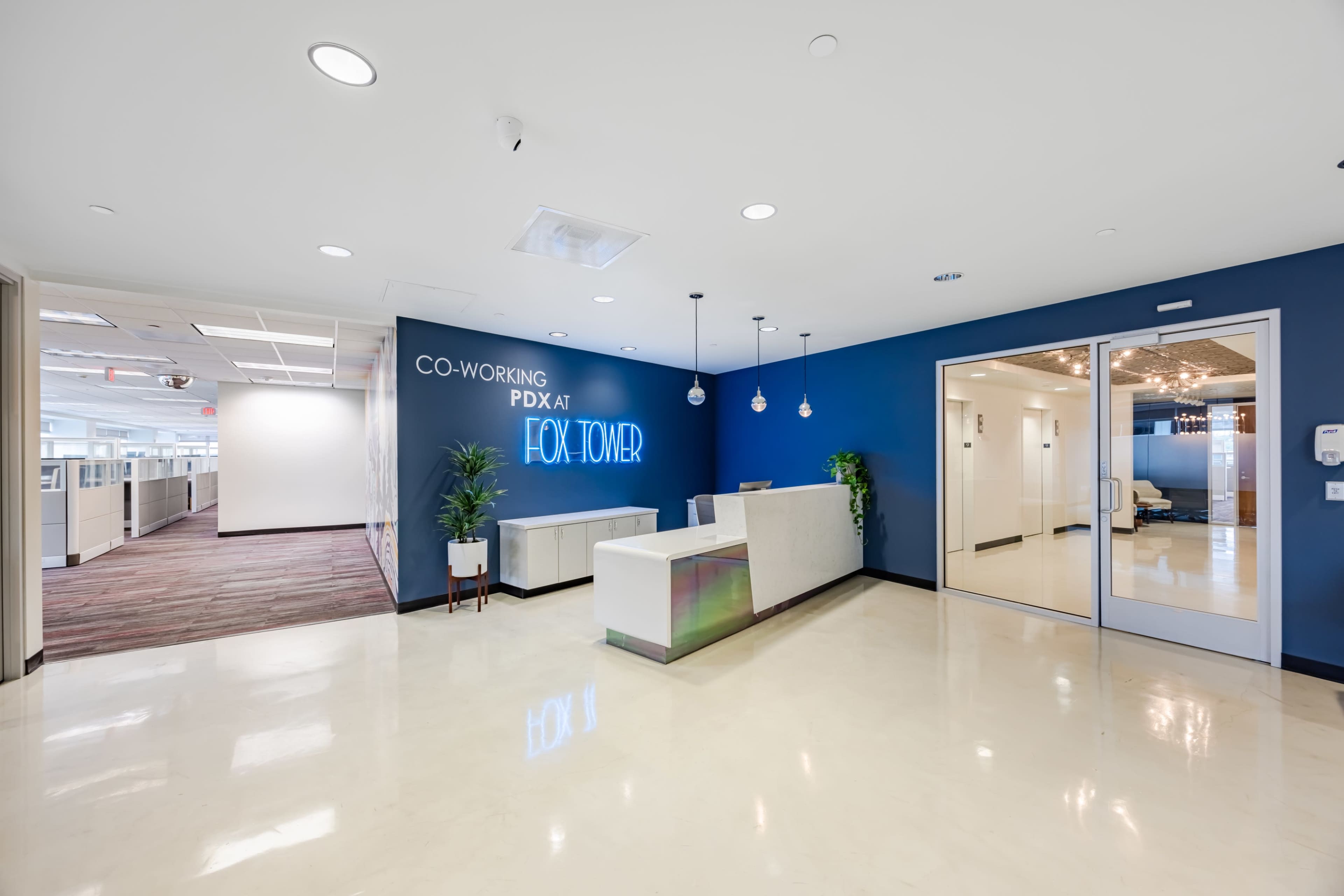 The image shows the reception area of a co-working space named Fox Tower, featuring a sleek white desk and a blue accent wall.