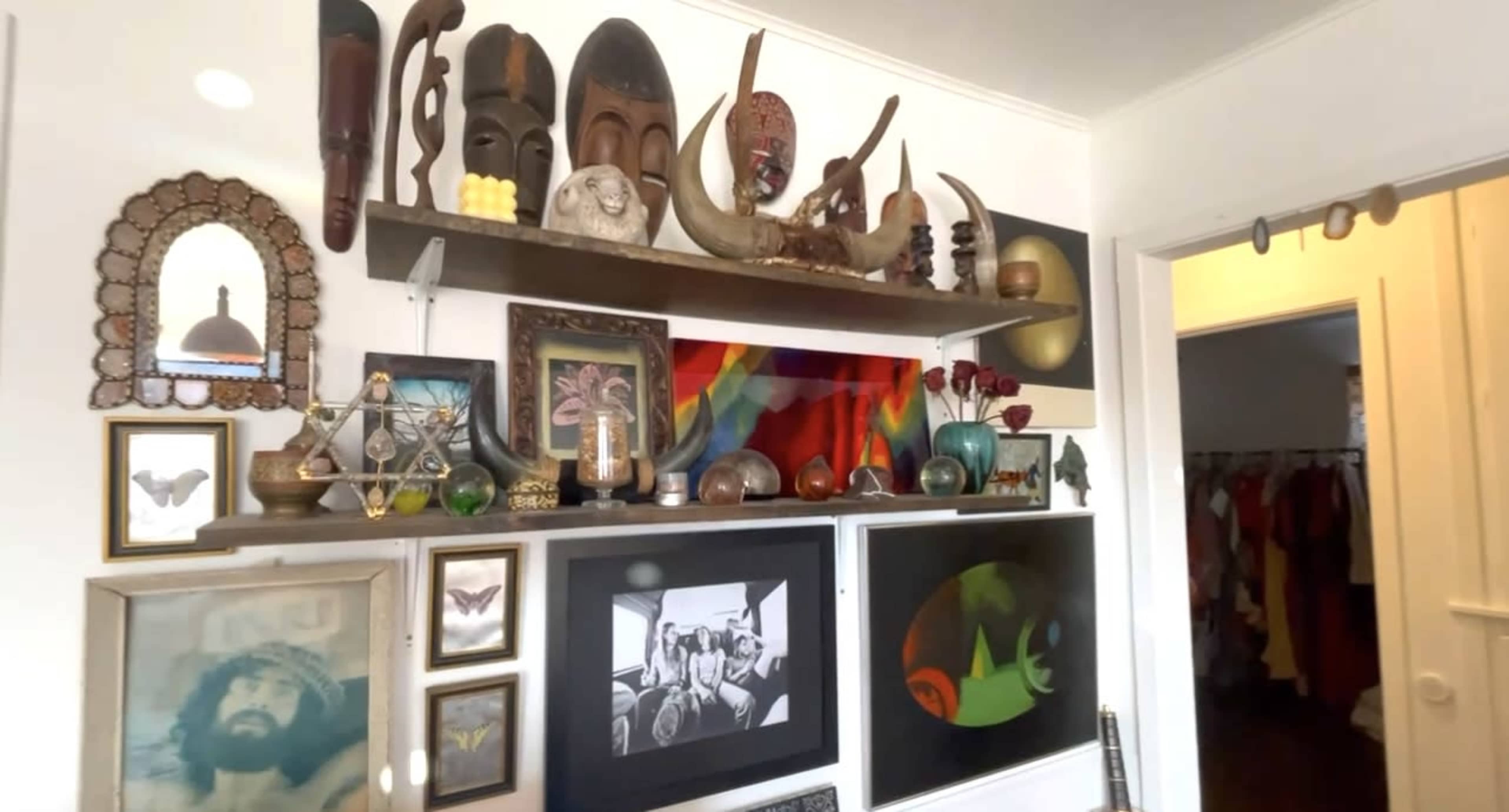 A wall adorned with a variety of masks, sculptures, framed artwork, and decorative objects arranged on shelves.