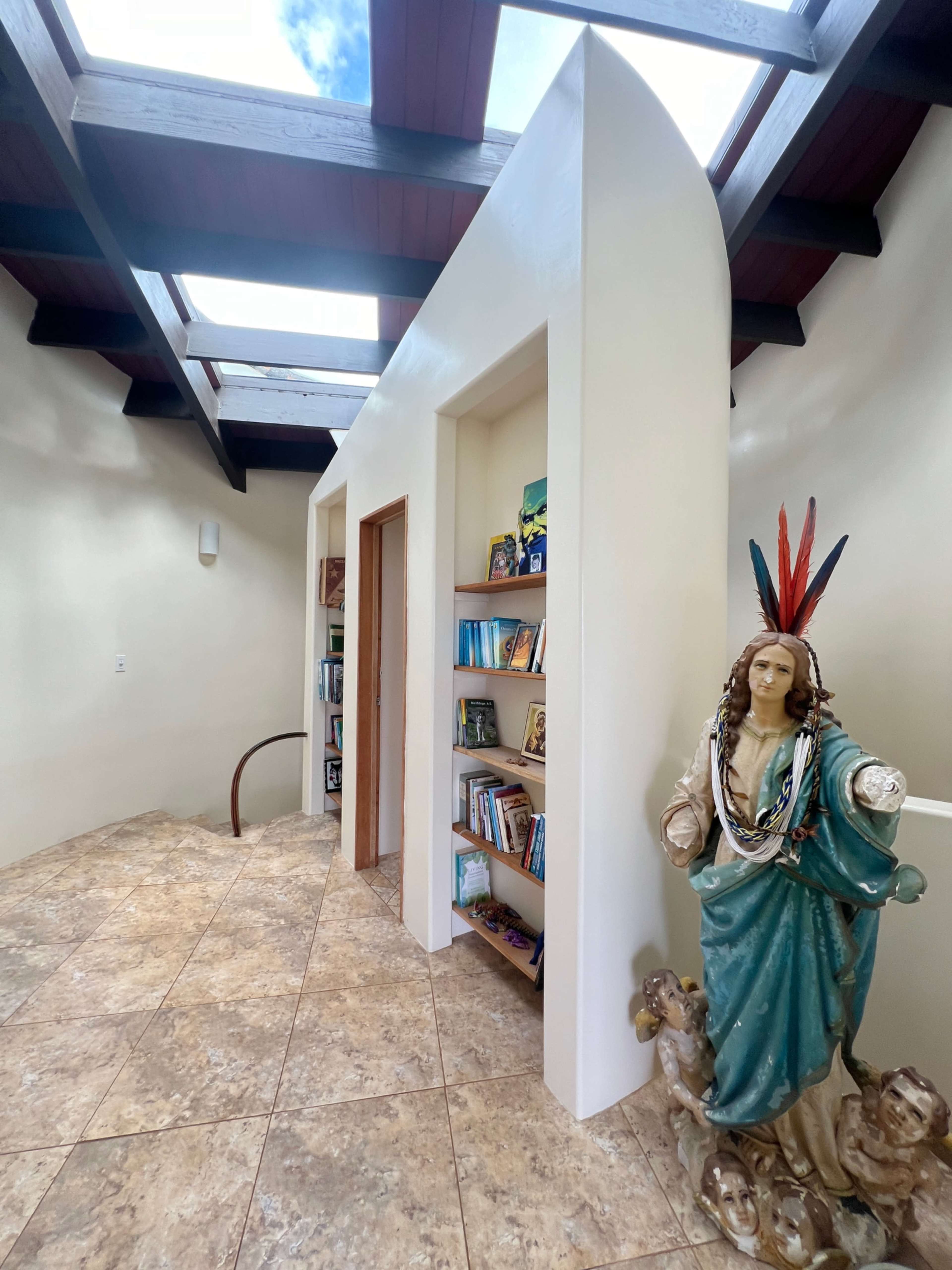 The image shows a well-lit interior space featuring a curved staircase, built-in bookshelves, and a decorative statue near the wall.