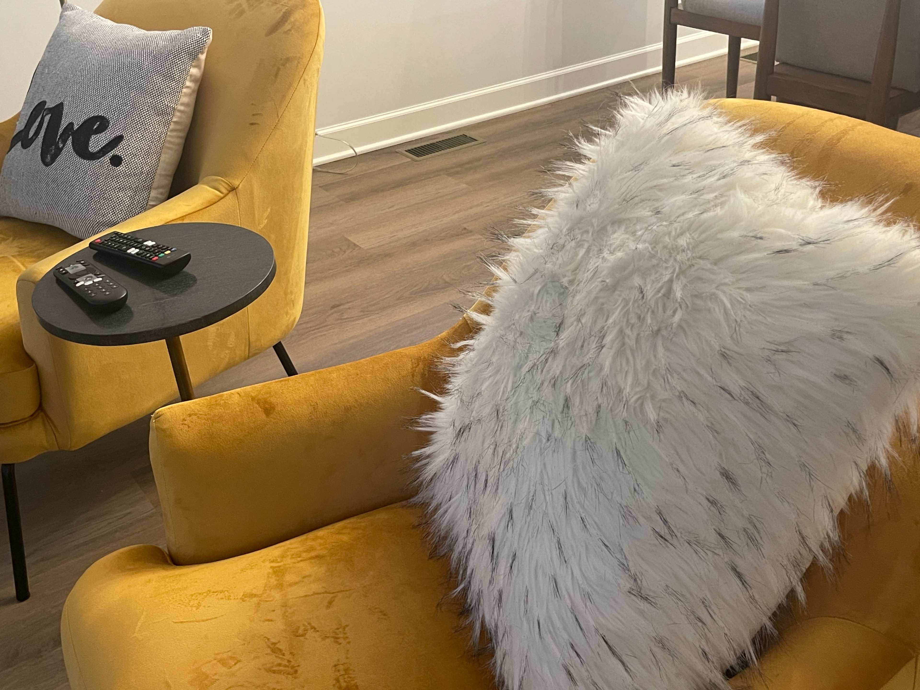 Two yellow armchairs, one adorned with a fluffy white pillow, next to a small black side table holding a remote control.