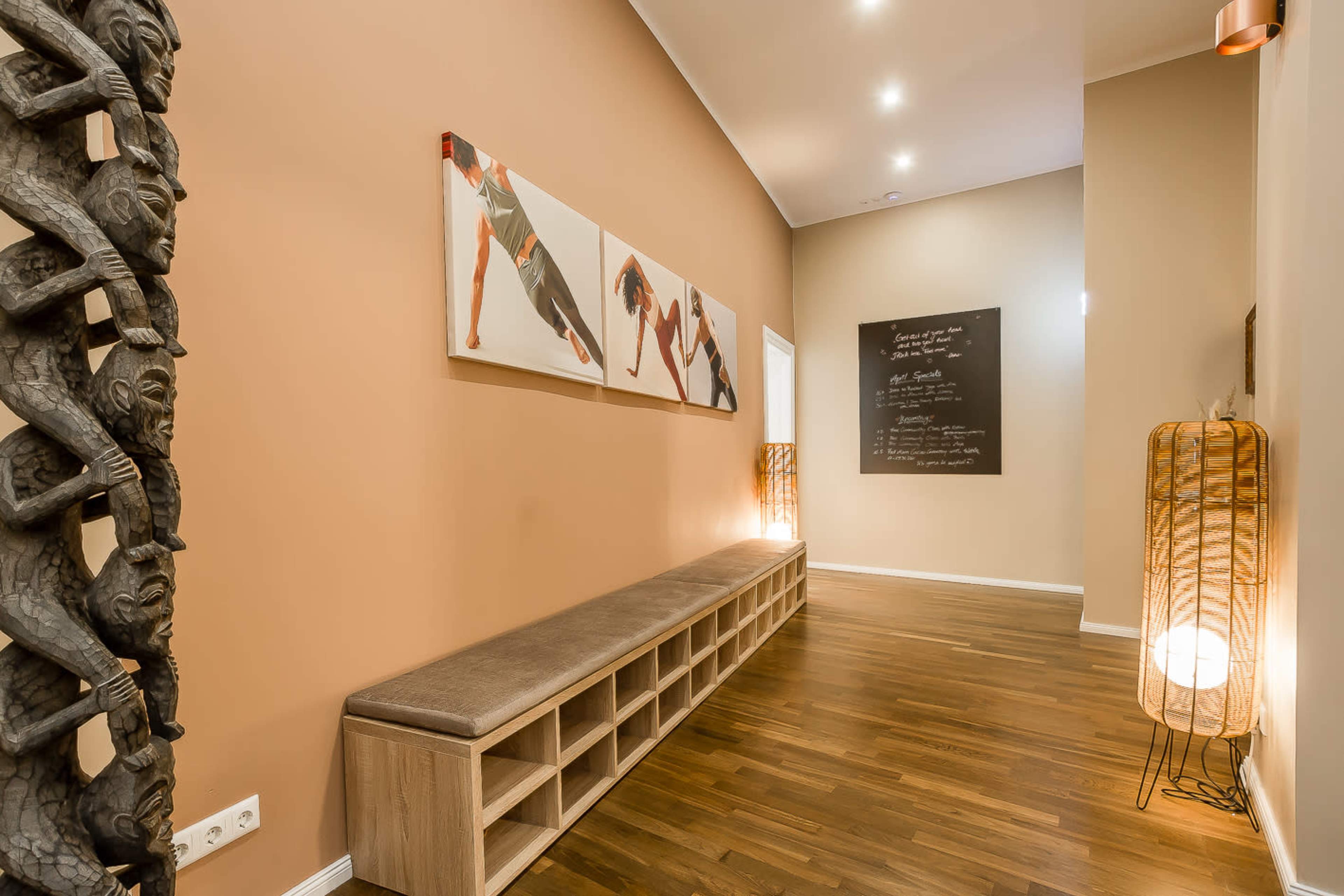 A hallway with wooden flooring, a carved wooden column, a bench, artwork on the wall, a chalkboard, and decorative lighting.