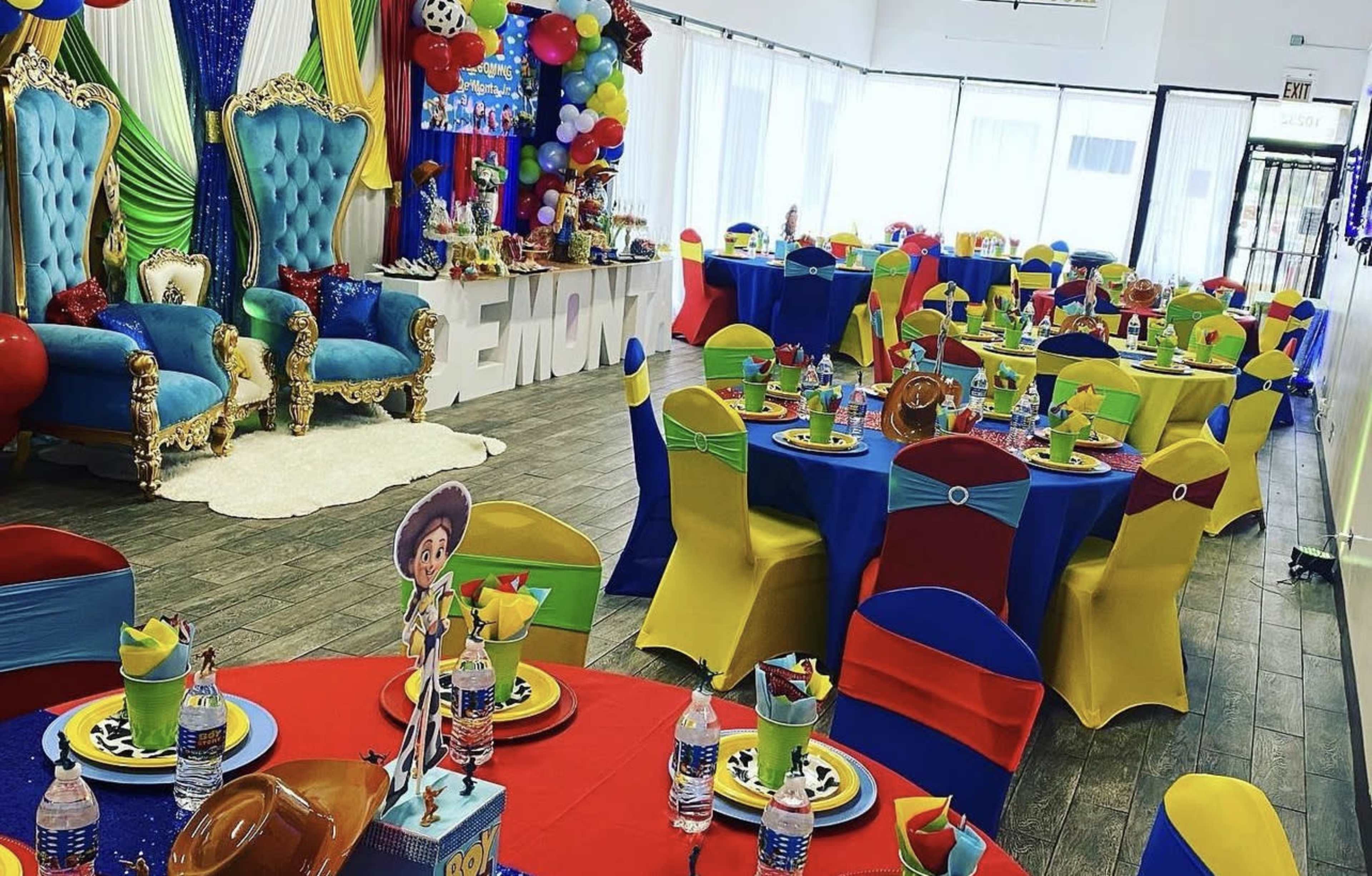 A colorful party venue decorated with blue and gold chairs, vibrant tablecloths in red, blue, yellow, and green, and festive balloons.