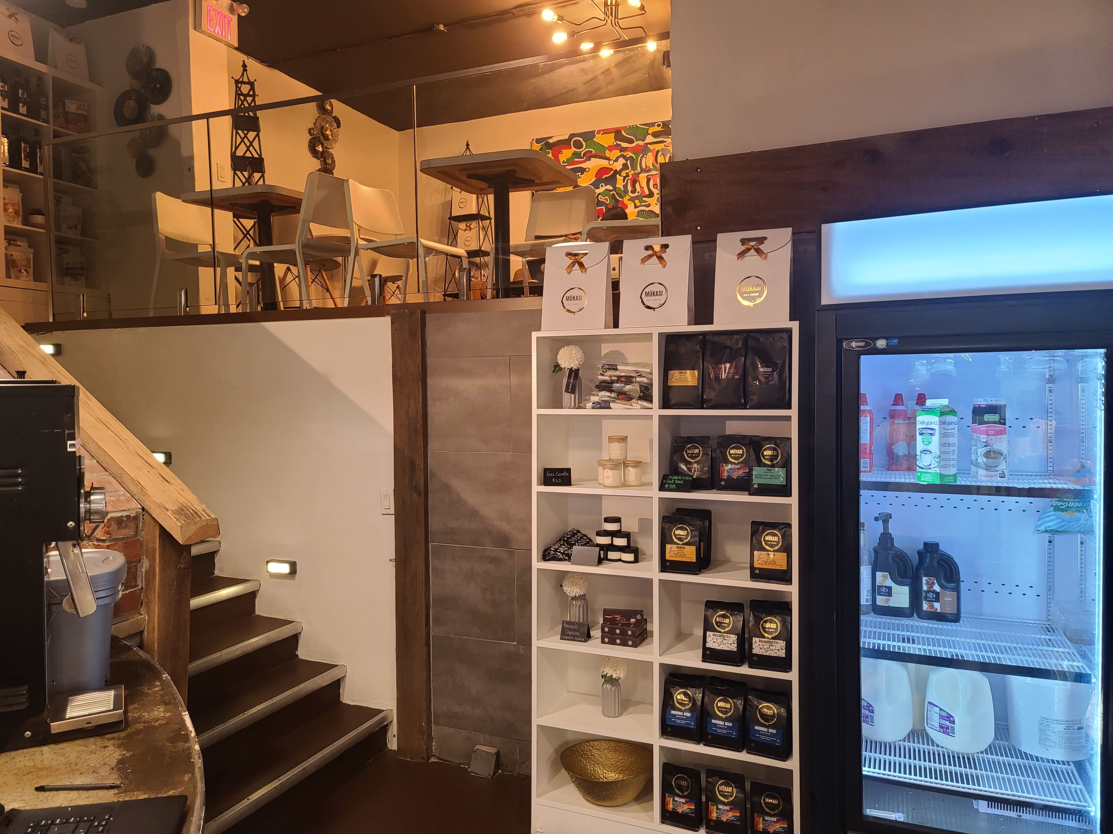 An interior of a café or store featuring a display shelf with products on one side and seating areas in the background.