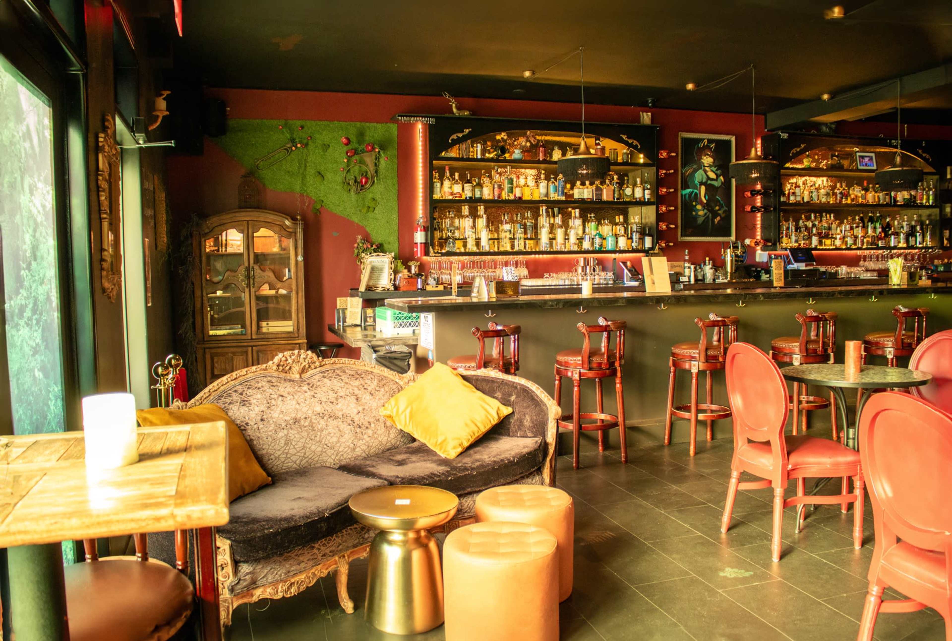 A cozy bar area features a dark countertop, wooden stools, red chairs, and a vintage couch with a yellow cushion.
