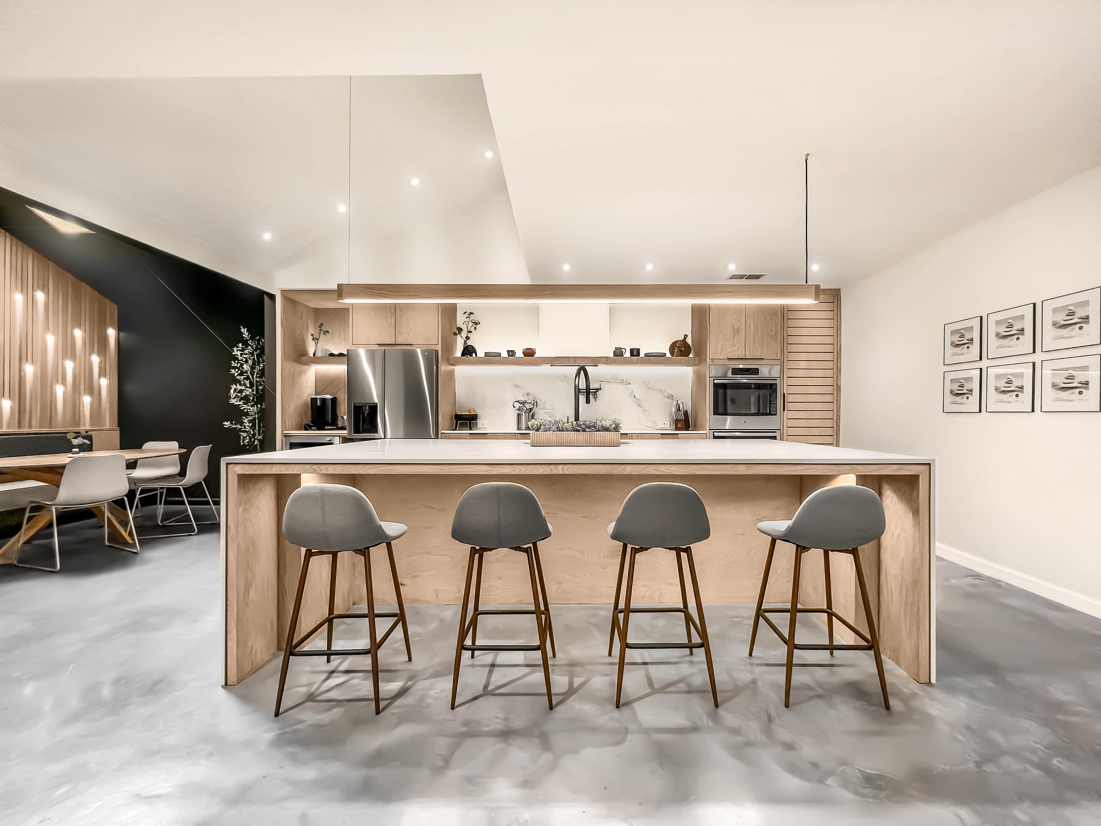 A modern kitchen with a central island, four bar stools, stainless steel appliances, and open shelving.