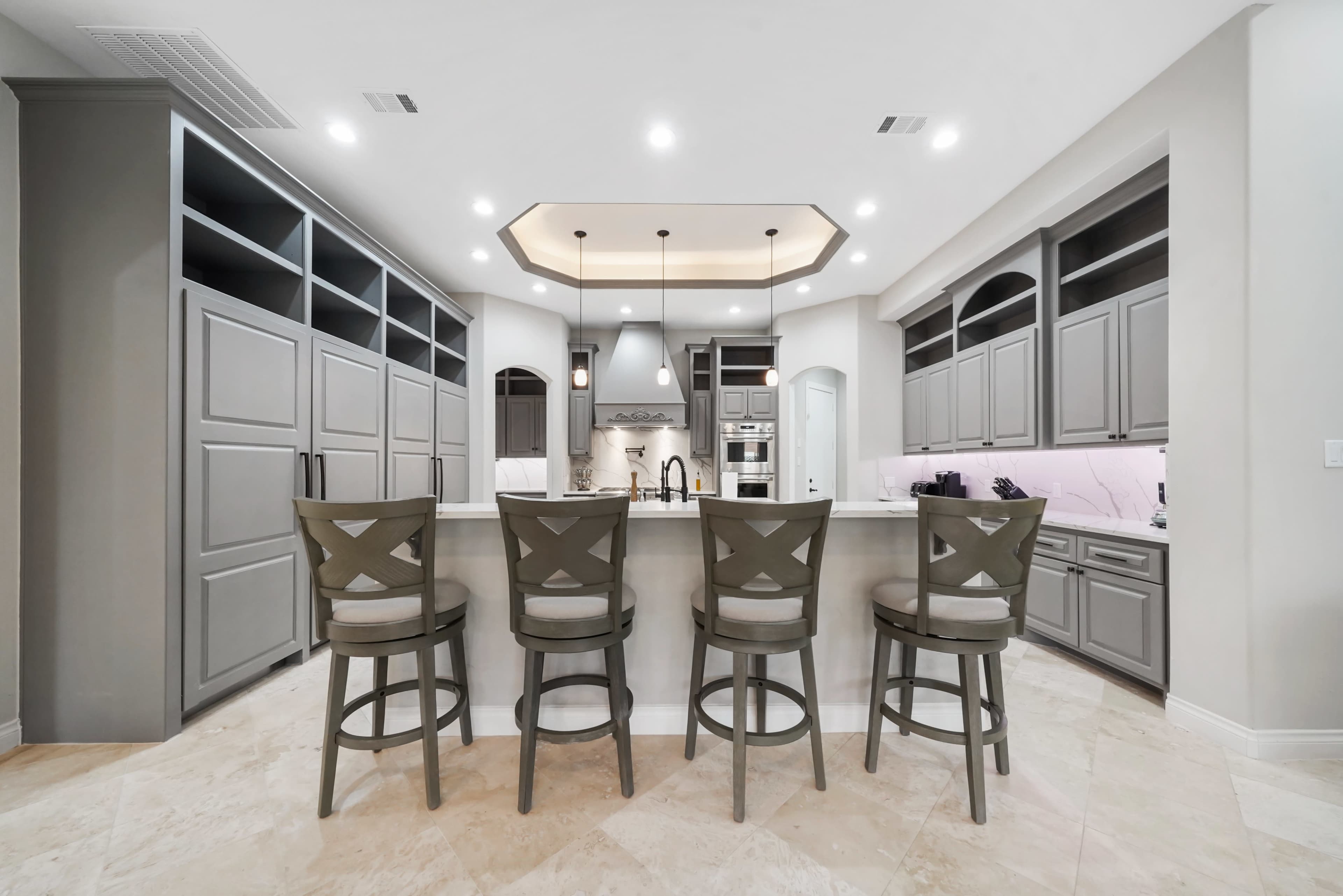 A modern kitchen features a central island with seating, surrounded by gray cabinetry and stainless steel appliances.