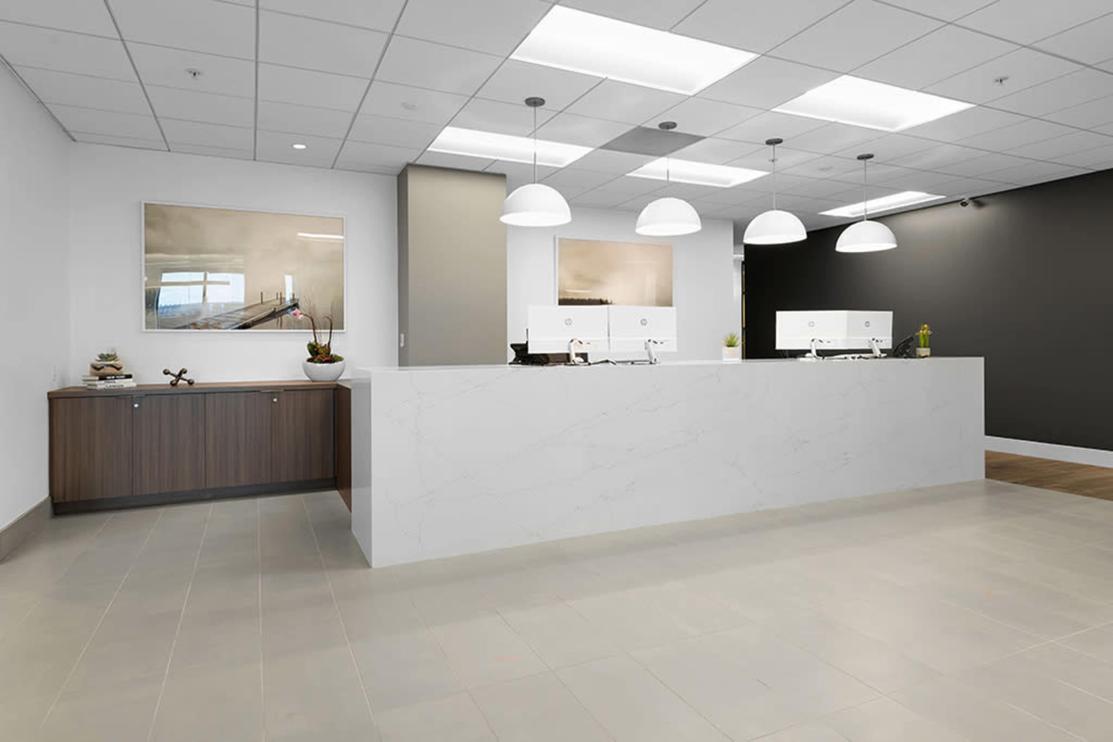 The image shows a modern reception area with a large white marble desk, pendant lighting, and abstract art on the walls.