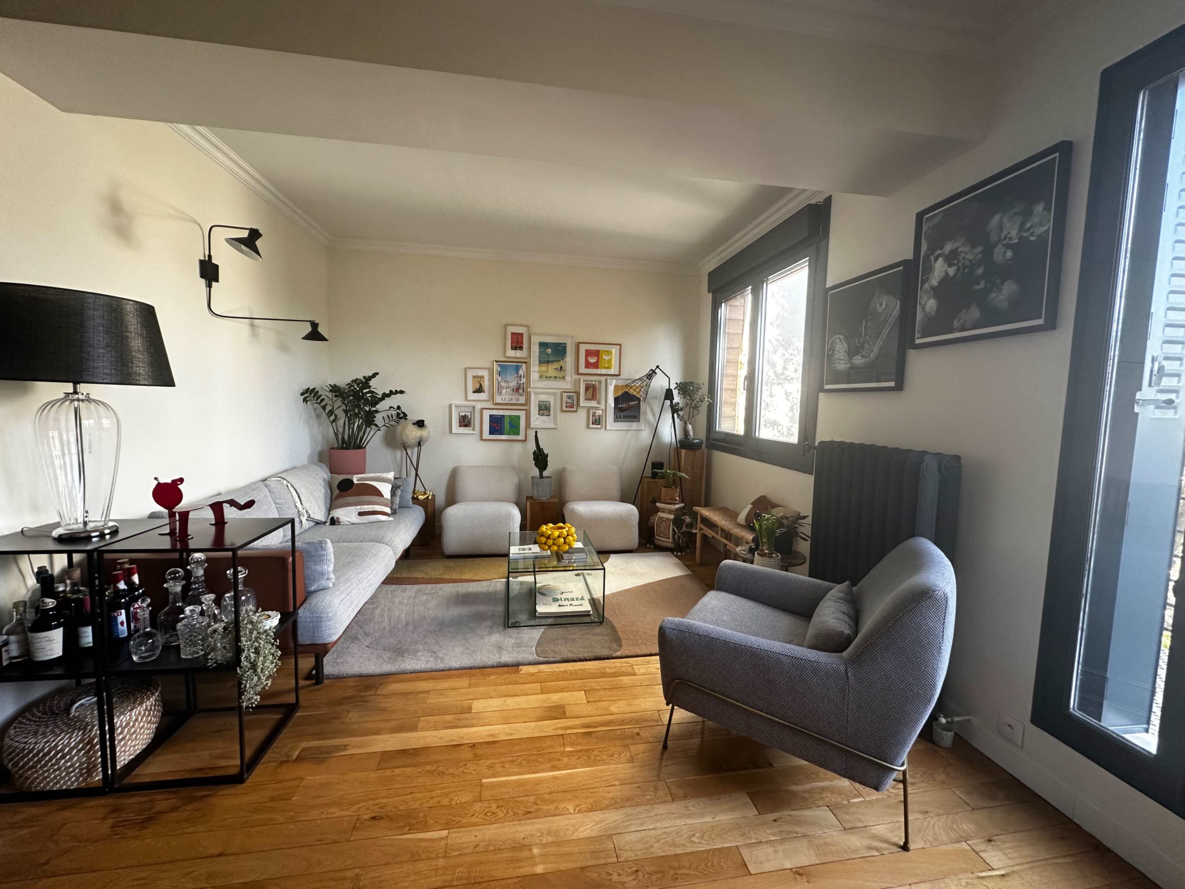 The image shows a living room with a gray sofa, a coffee table, a collection of framed pictures on the wall, and various decorative items.