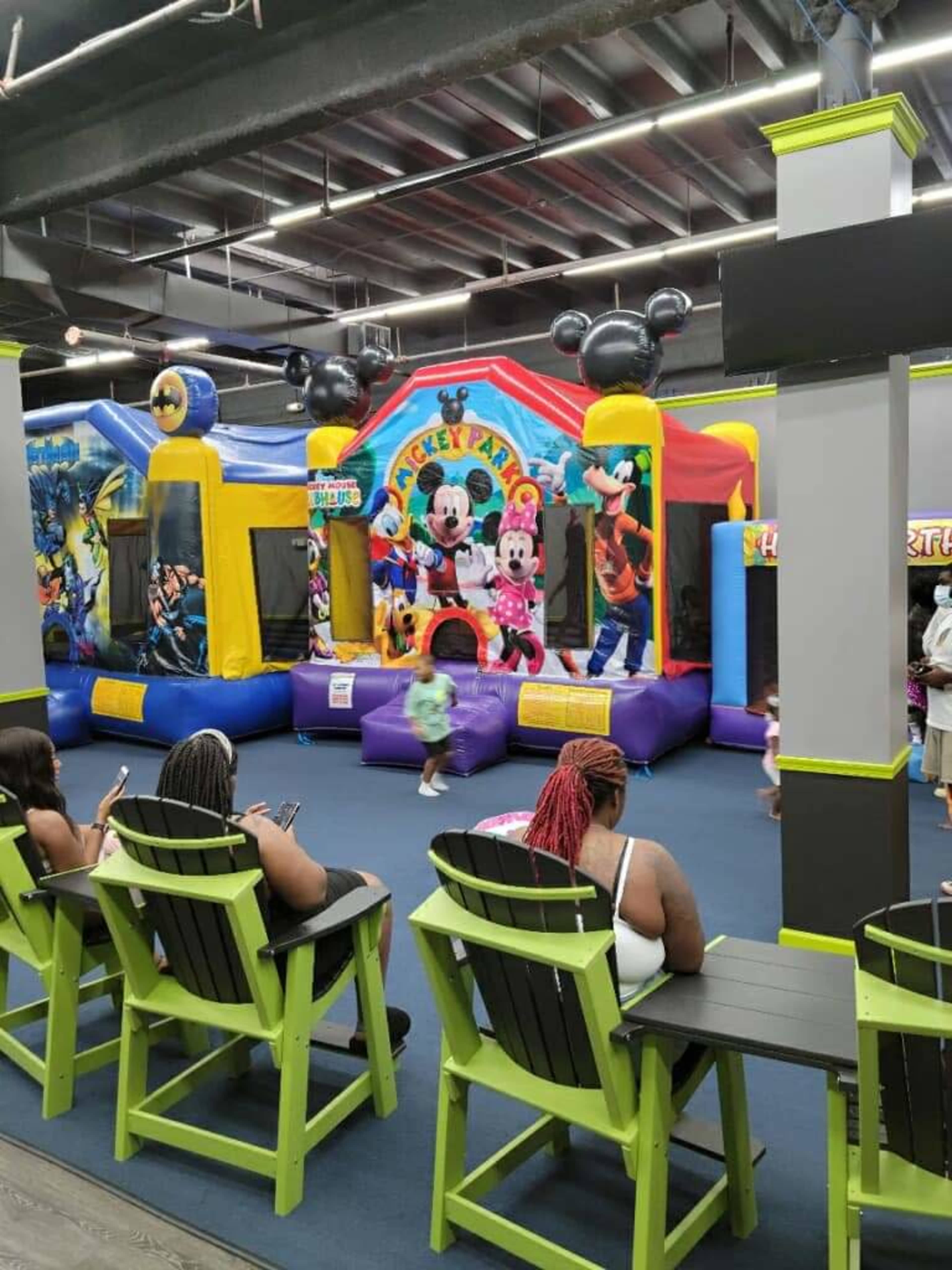 Several colorful bounce houses in a playground area, with children playing inside while adults sit on chairs nearby.