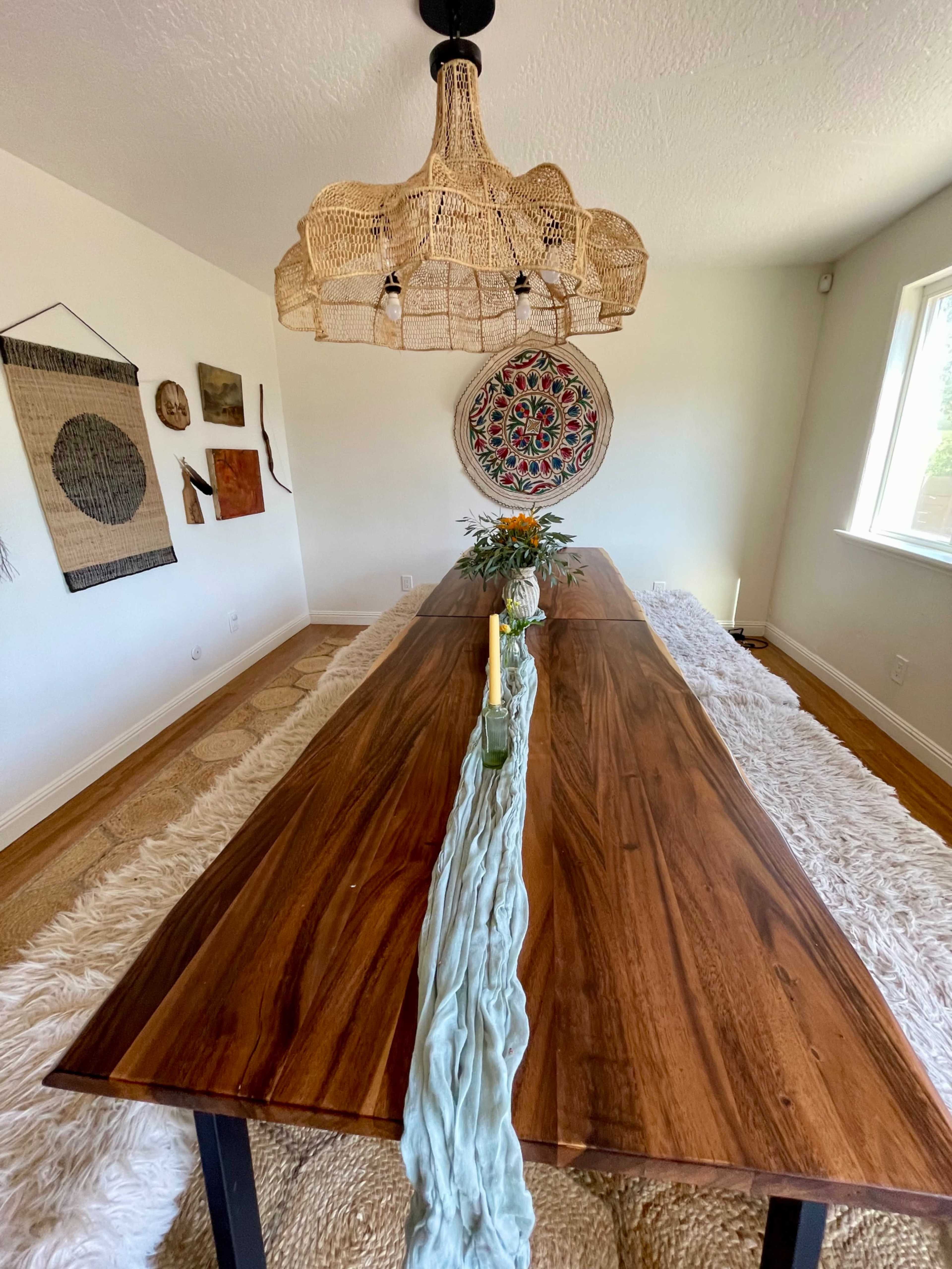 The image shows a spacious dining room with a long wooden table, topped with a centerpiece, and a large woven light fixture hanging overhead.