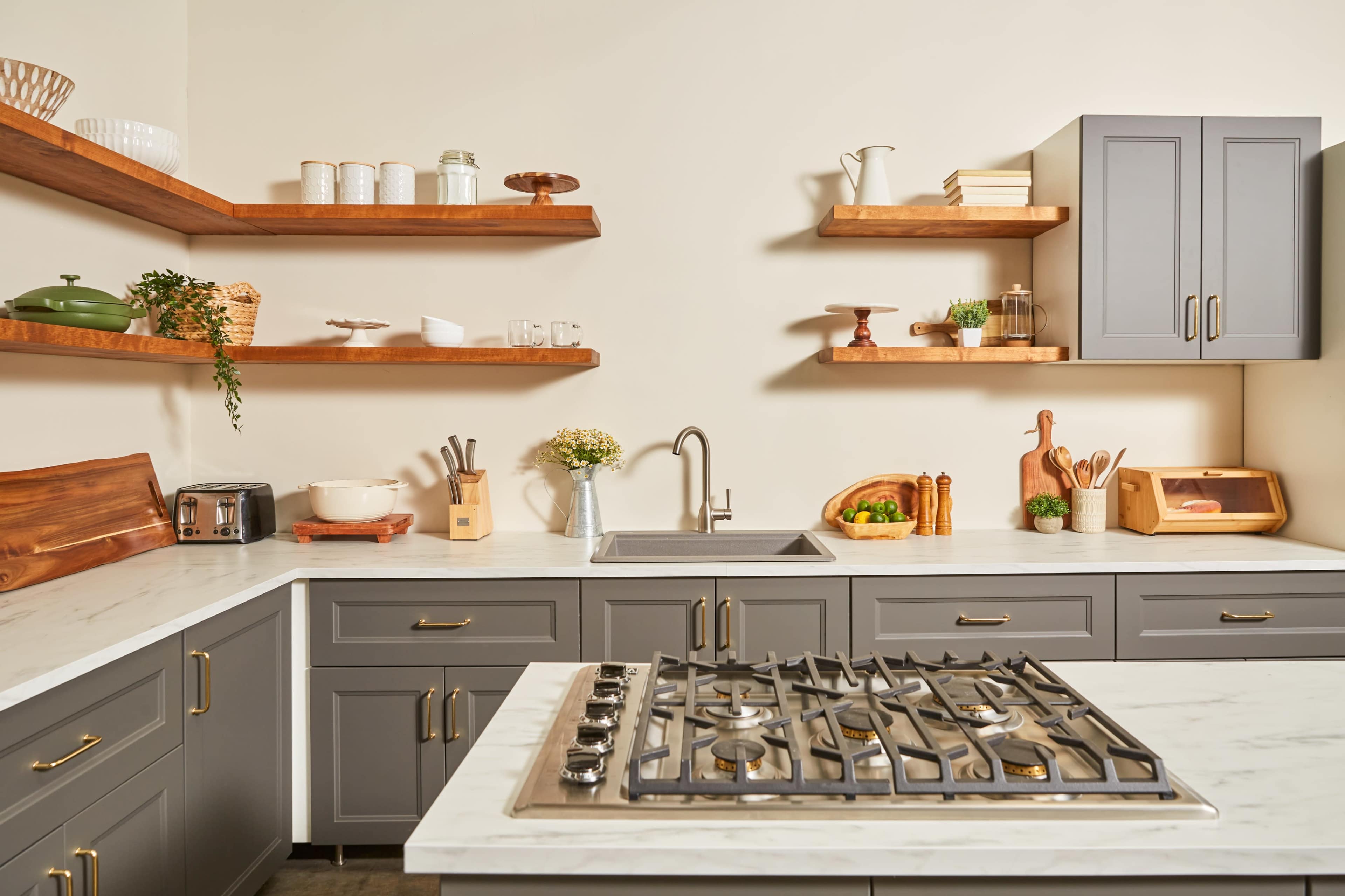 The kitchen features gray cabinetry with wooden shelves displaying various kitchen items, a stainless steel sink, and a gas stove set into a marble countertop.