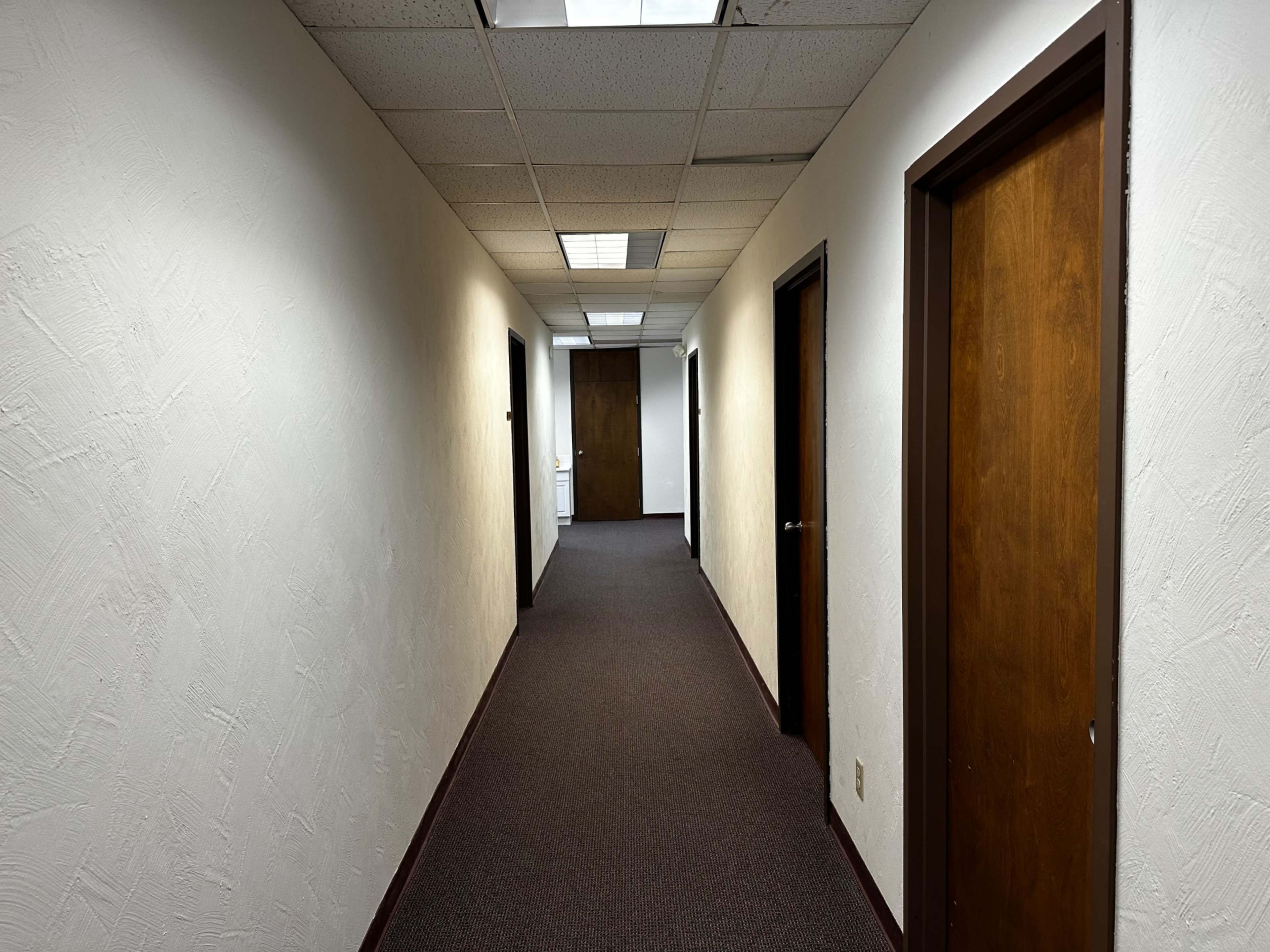 The image shows a long, narrow hallway with several doors on either side and a light ceiling above.