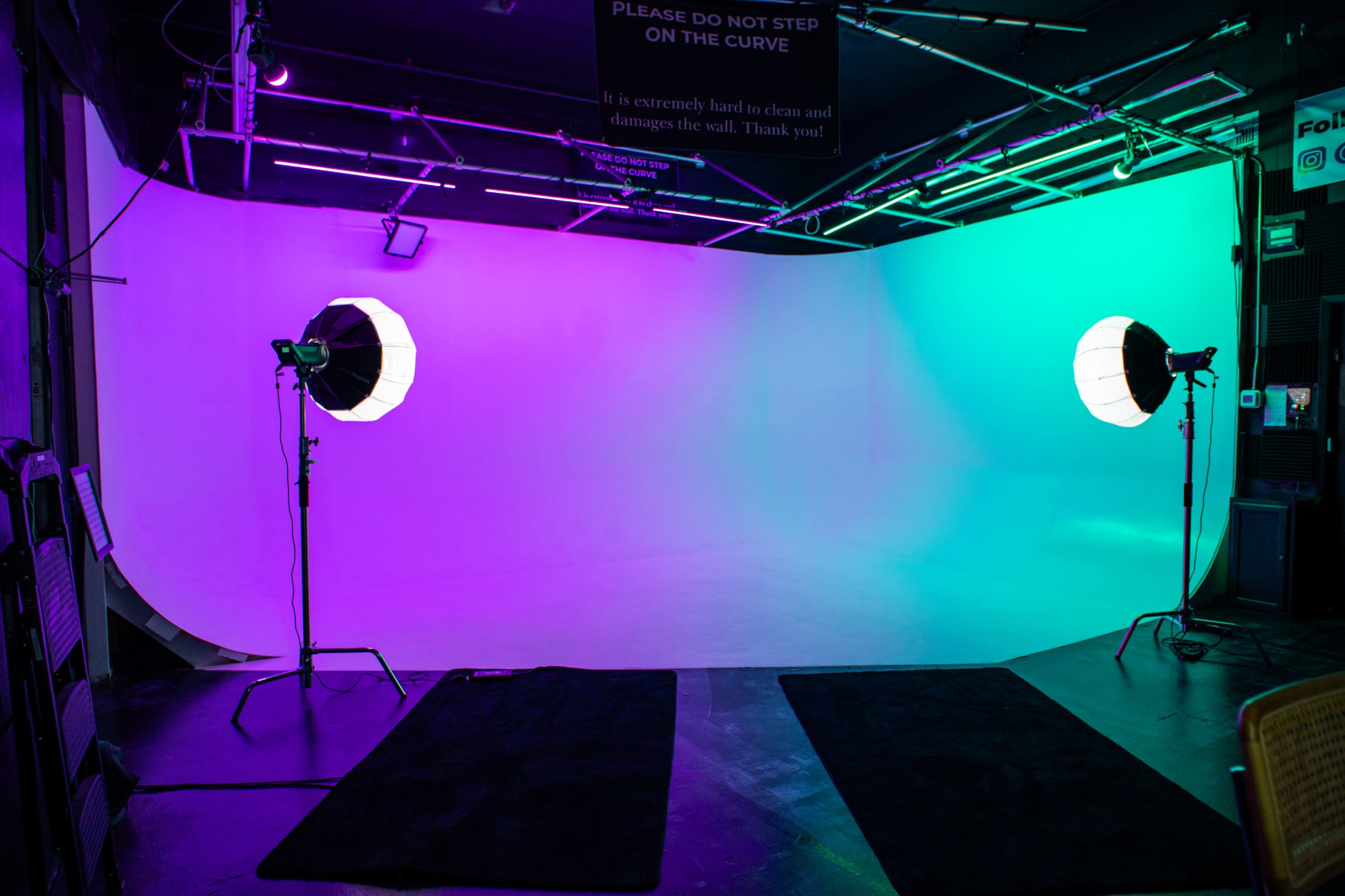 The image shows a photography studio with a seamless backdrop lit in vibrant colors, two softbox lights positioned on either side, and a notice sign above.