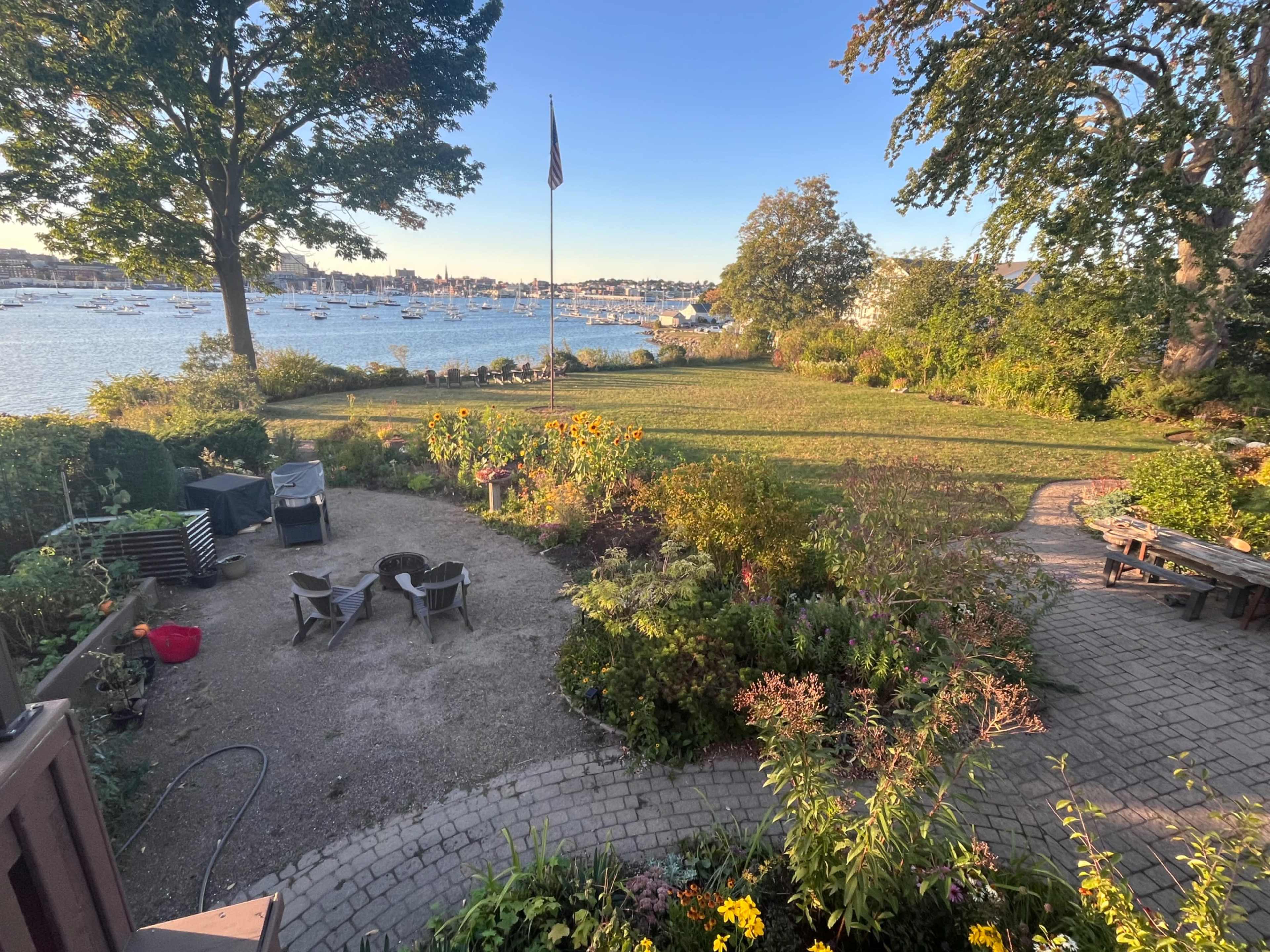 A landscaped garden with a grassy area and seating, overlooking a harbor filled with boats and a flagpole in the background.