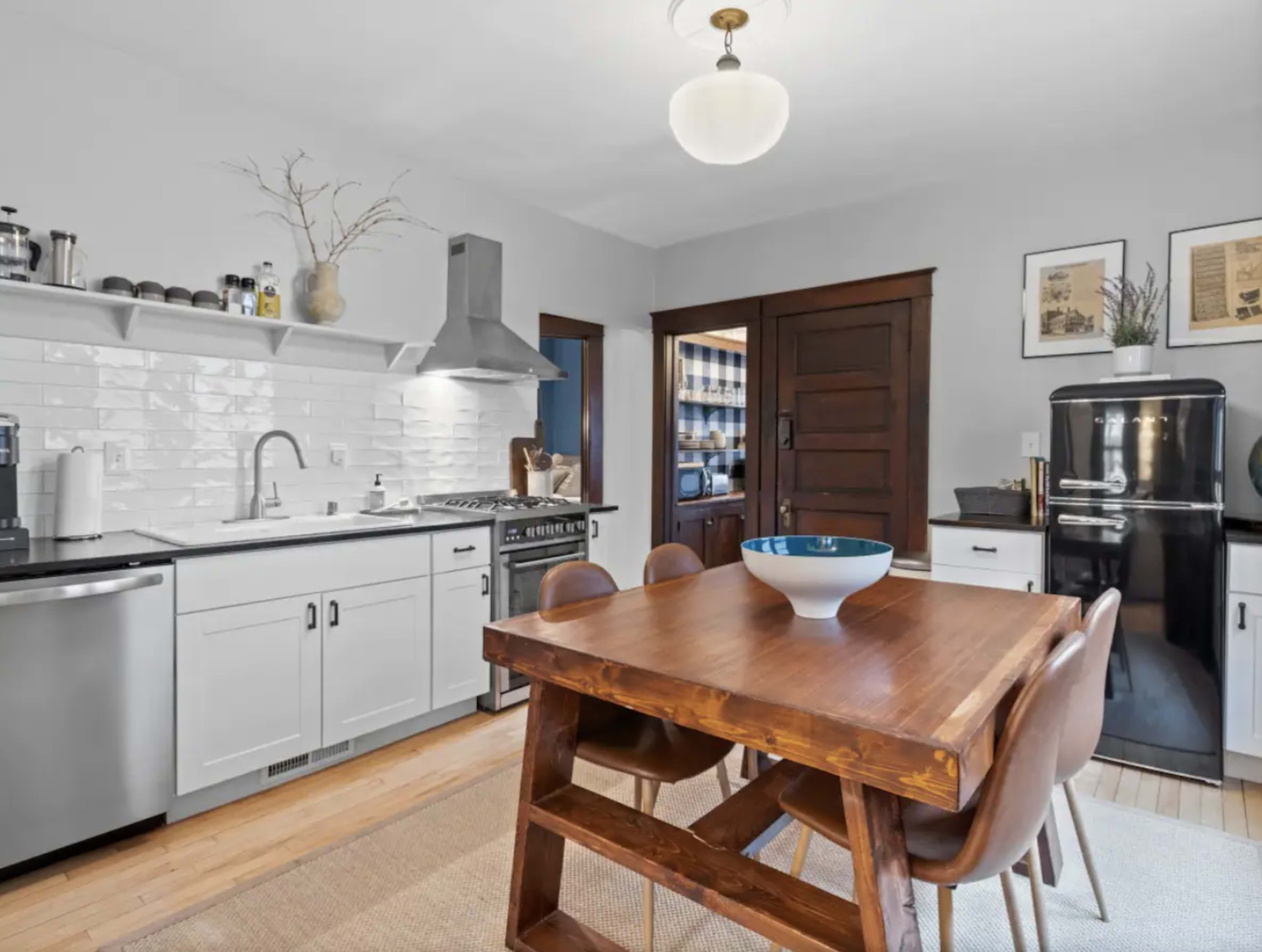 A modern kitchen features white cabinetry, stainless steel appliances, and a wooden dining table with brown chairs.