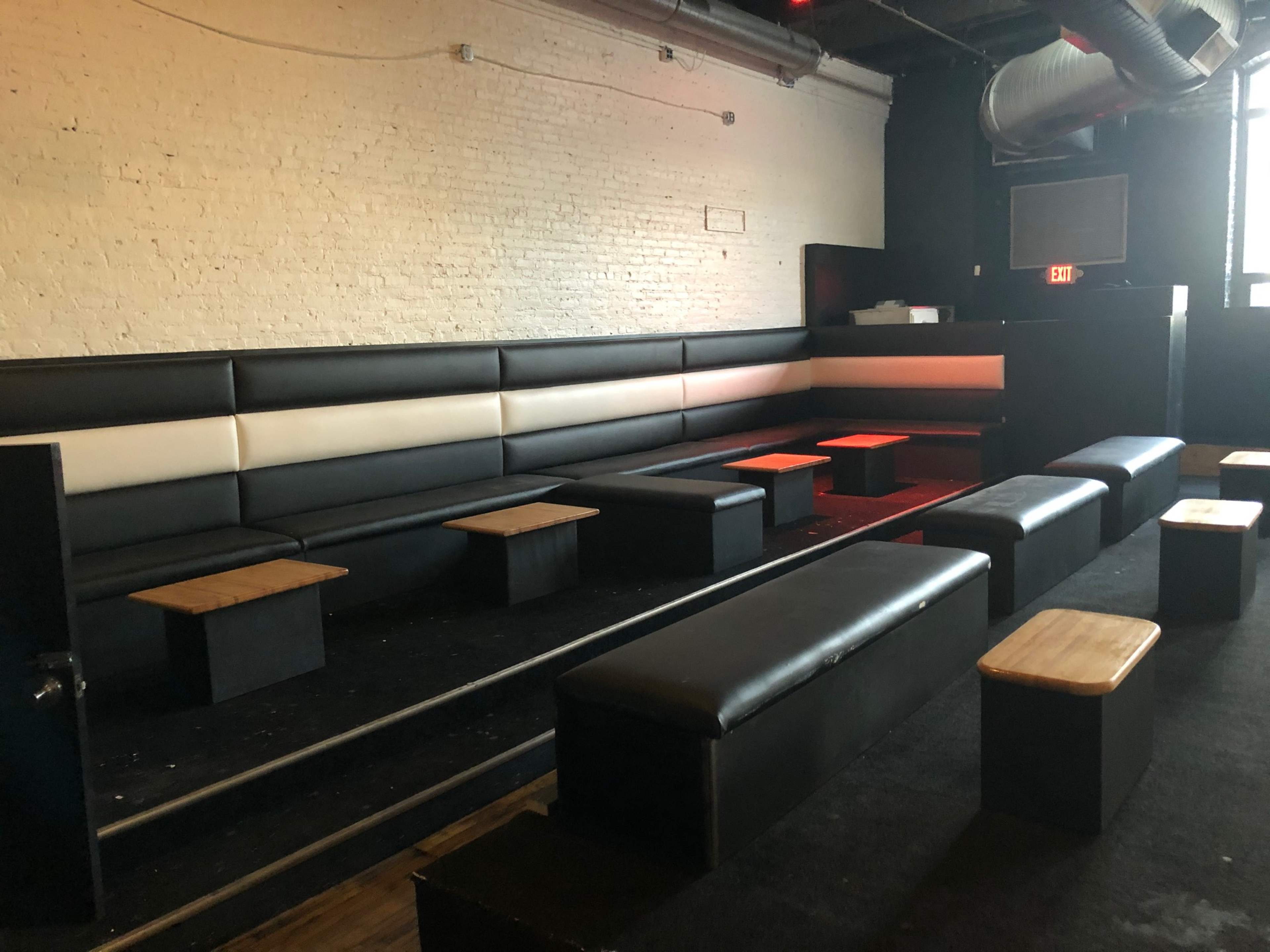 A dimly lit lounge area with black leather seating and wooden tables arranged in rows.