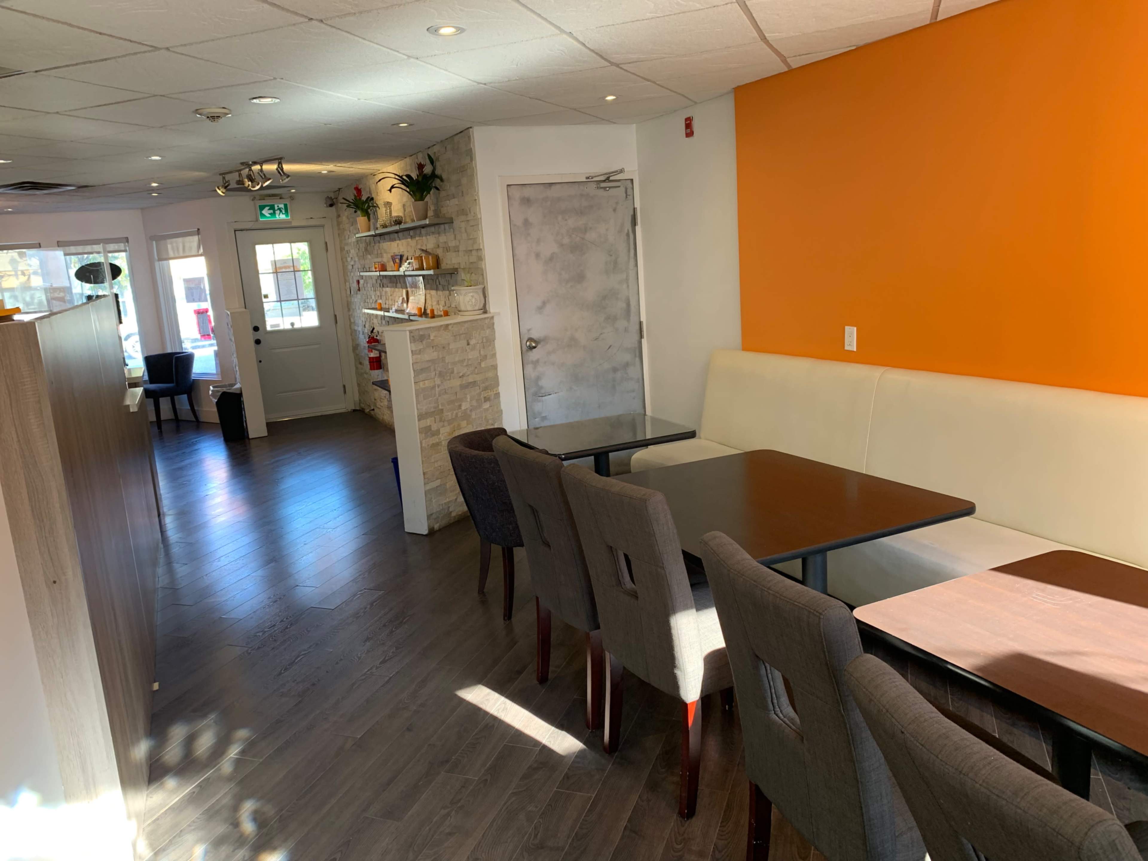 The interior of a restaurant with wooden floors, orange walls, and a row of tables and chairs along one side.