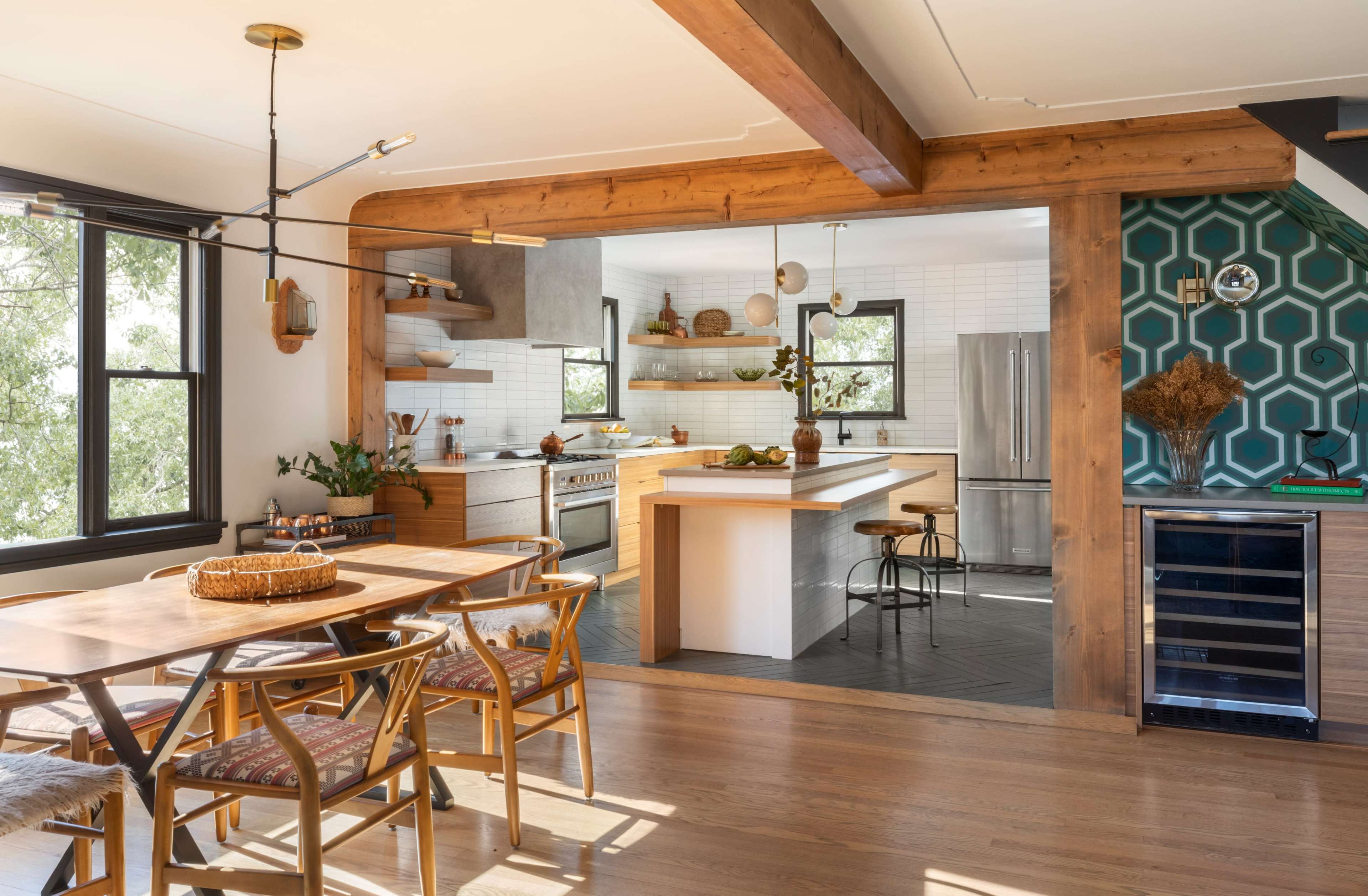 The image shows a modern kitchen and dining area with wooden beams, stylish cabinetry, and a dining table set for a meal.