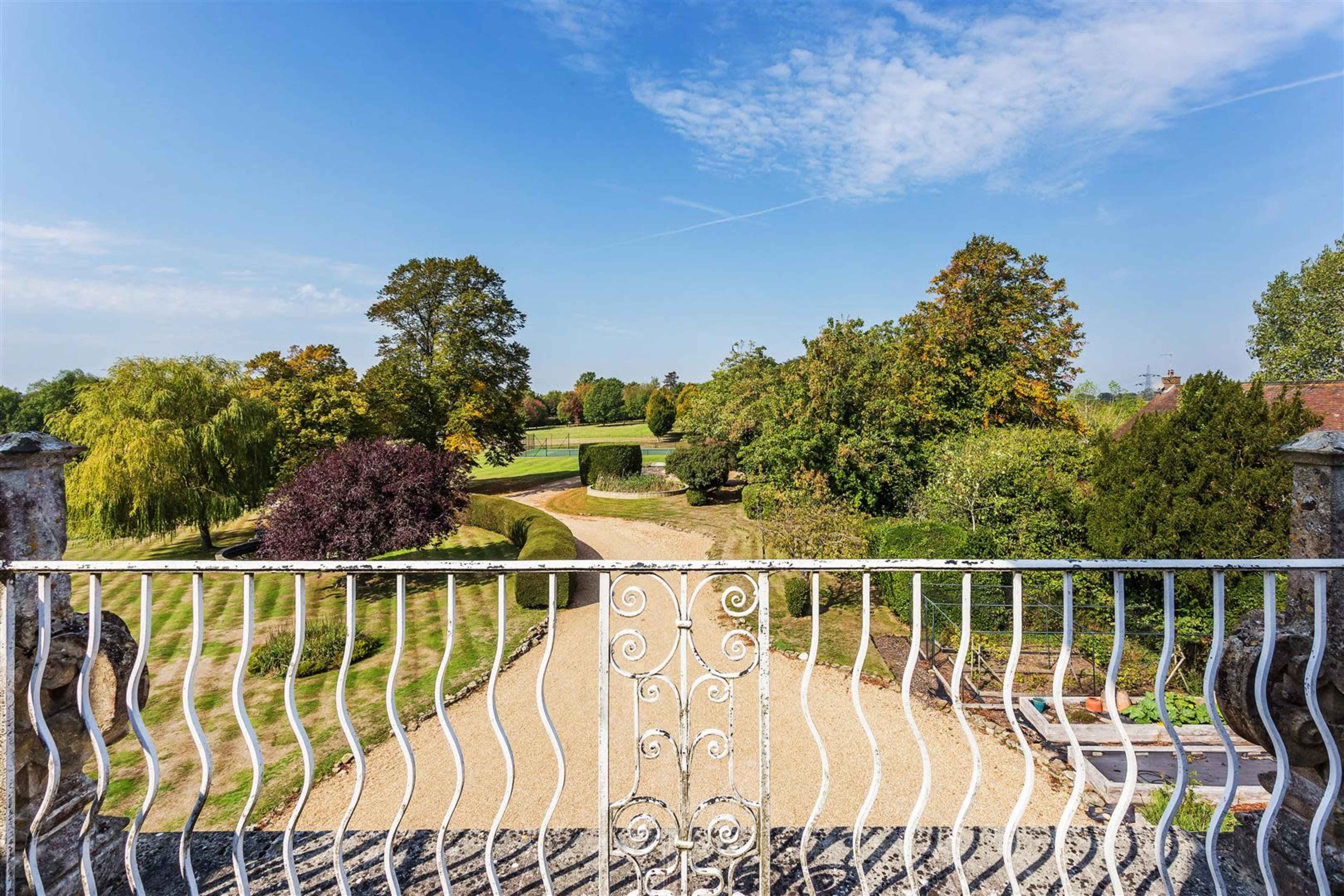 A wrought iron railing overlooks a landscaped garden with trees and a gravel pathway under a clear blue sky.