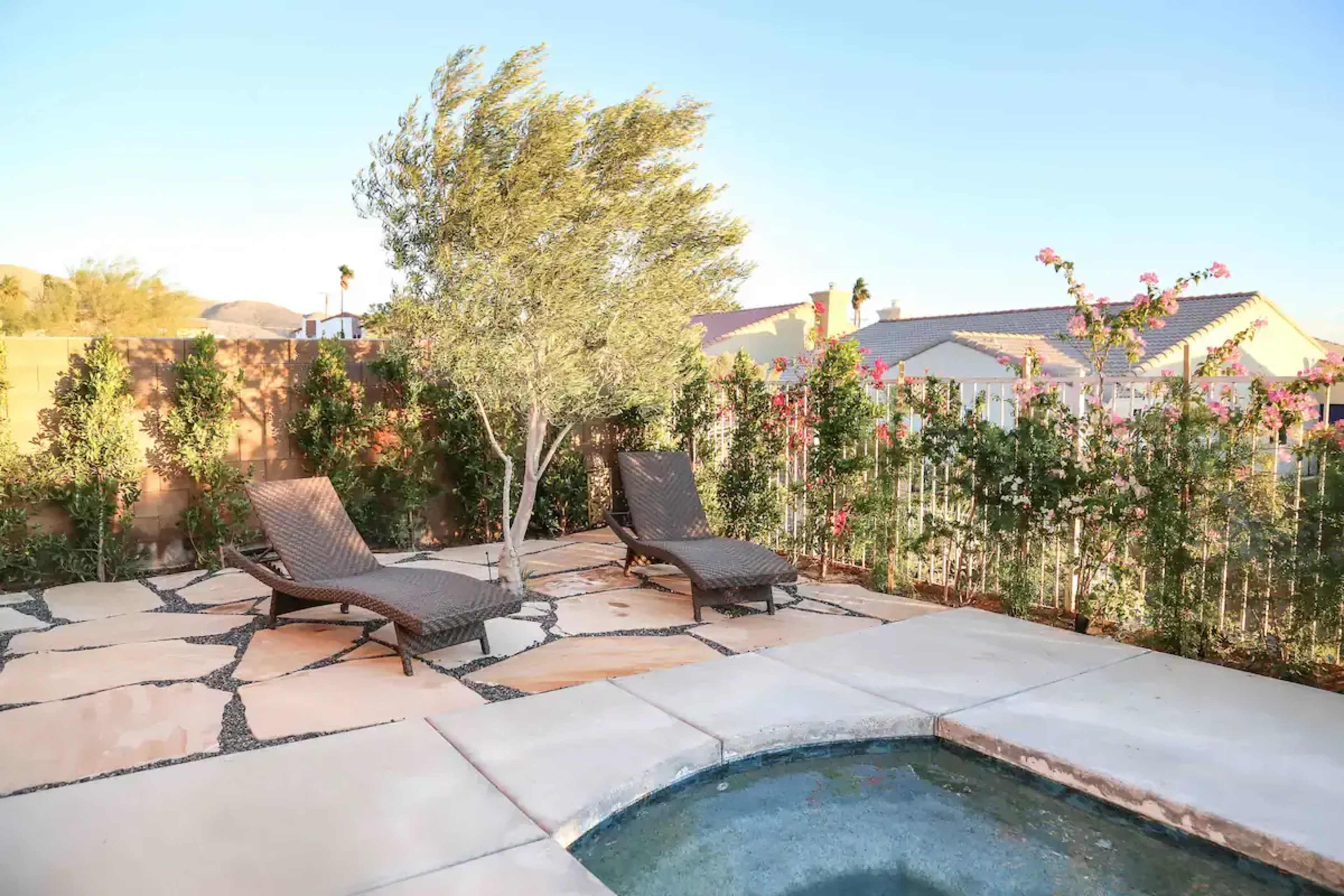 The image shows a landscaped backyard with two lounge chairs beside a small pool, surrounded by garden plants and a fence.