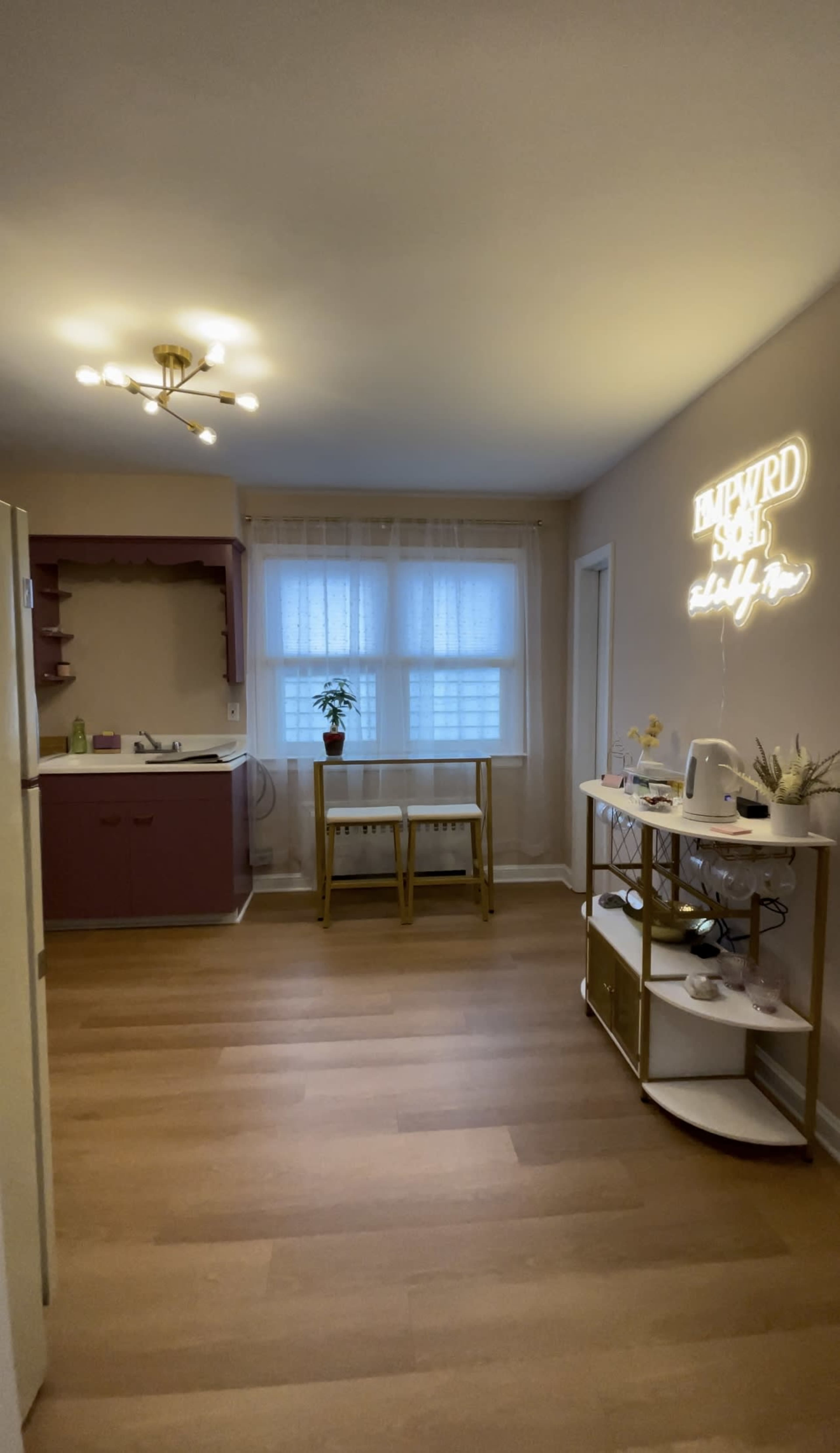 A bright, minimalistic kitchen and dining area features a wooden table, an open shelf, and a neon sign on the wall.