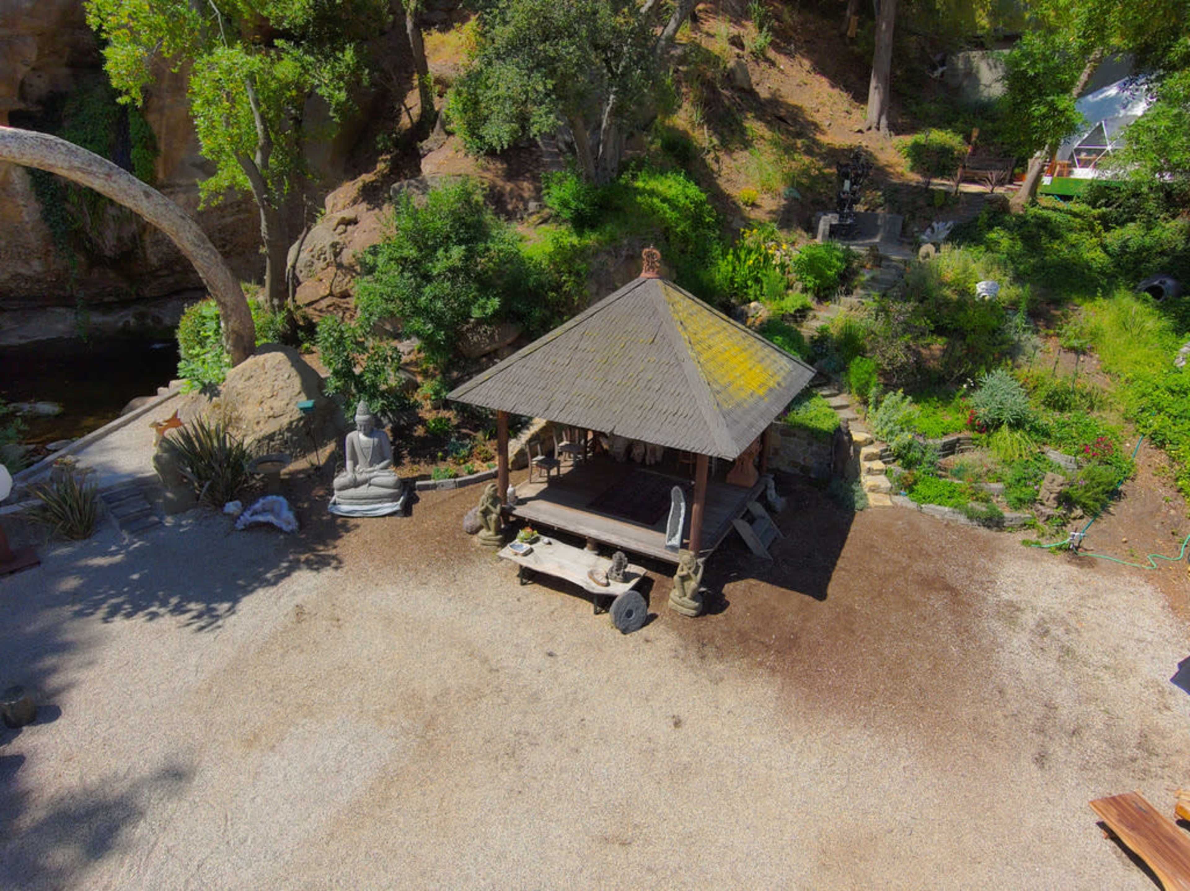 The image shows a gazebo surrounded by greenery and sculptures in a landscaped outdoor area.