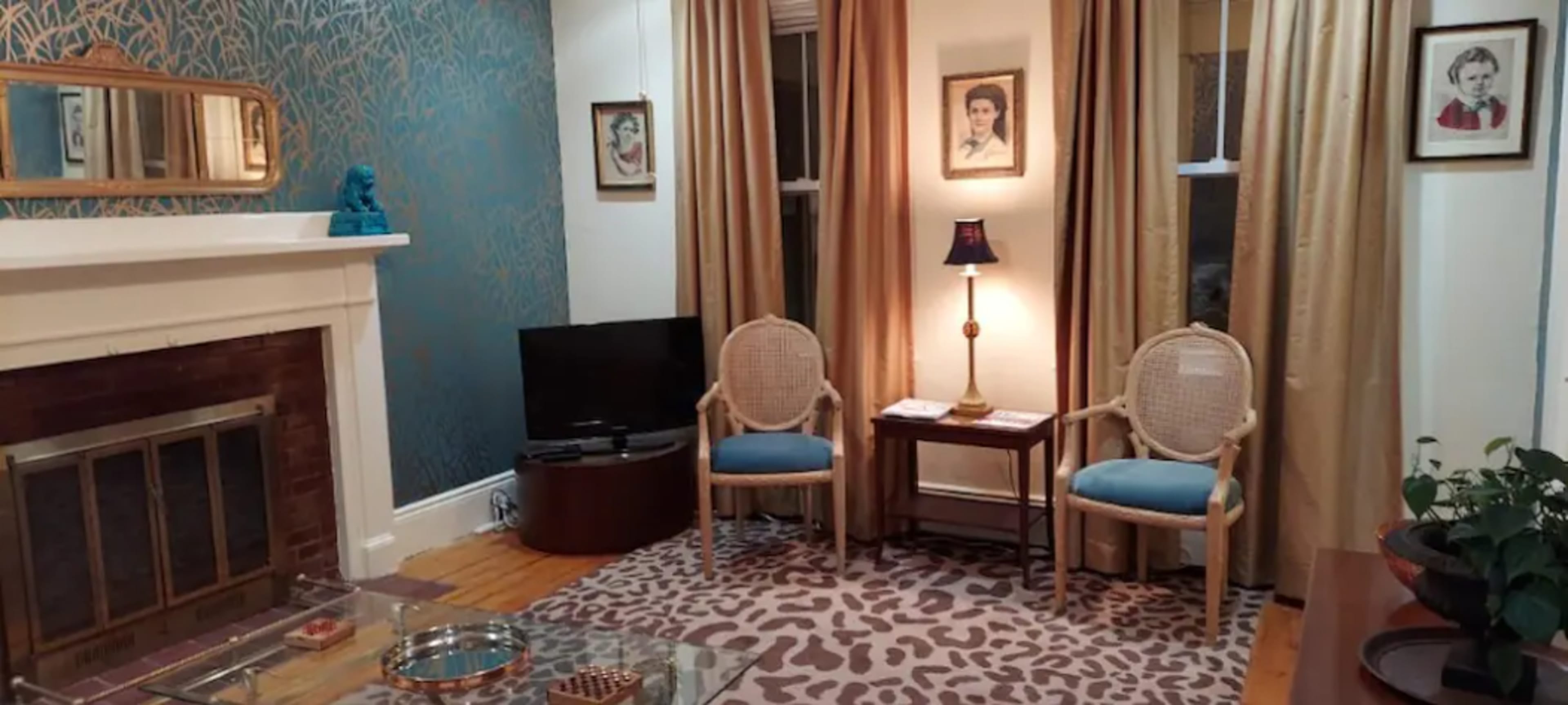 The room features a fireplace, two chairs with blue cushions, a television, and a pattern of animal-print decor on the floor.