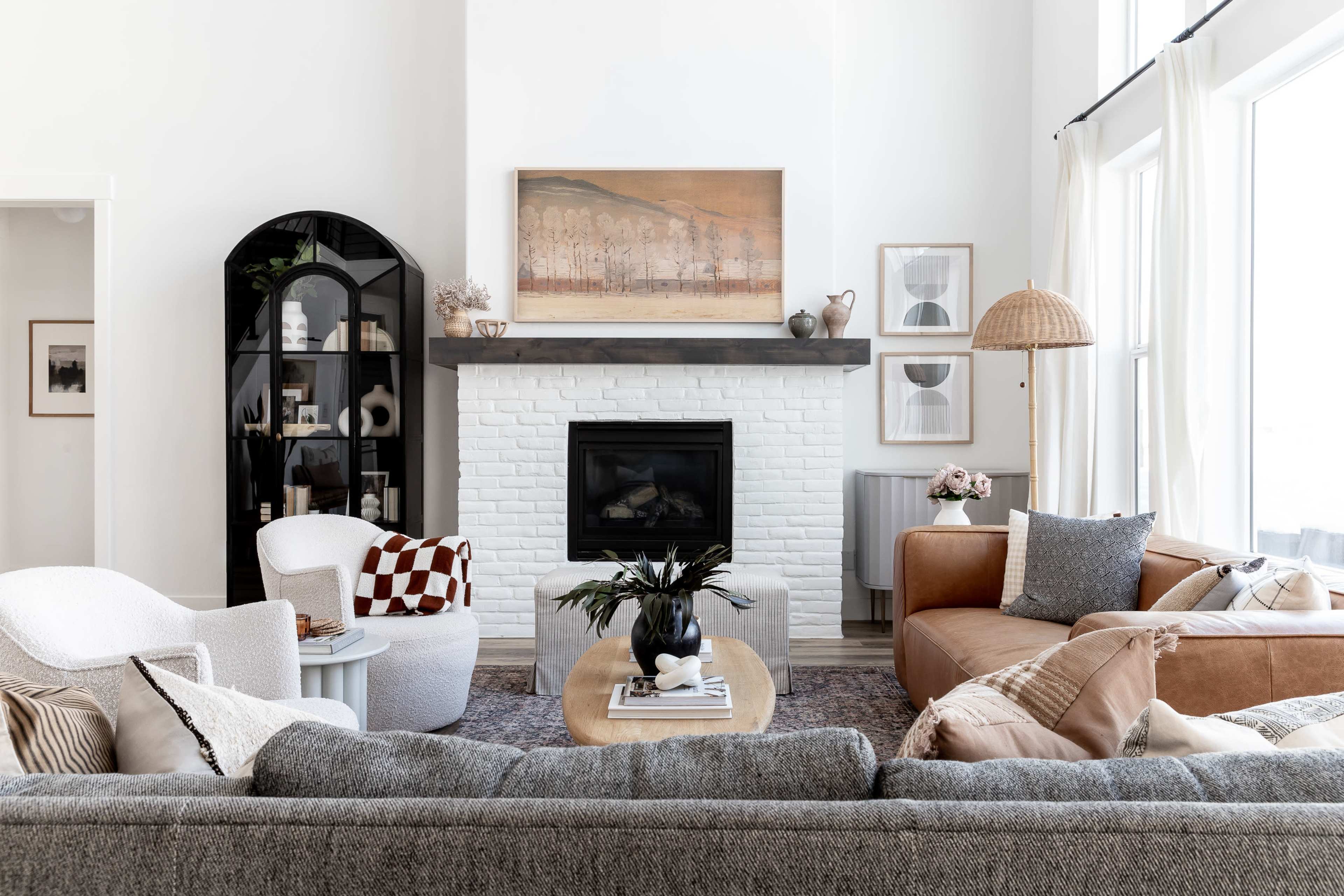 A spacious living room features a white-brick fireplace with a mounted artwork above it, surrounded by various seating options and a coffee table.