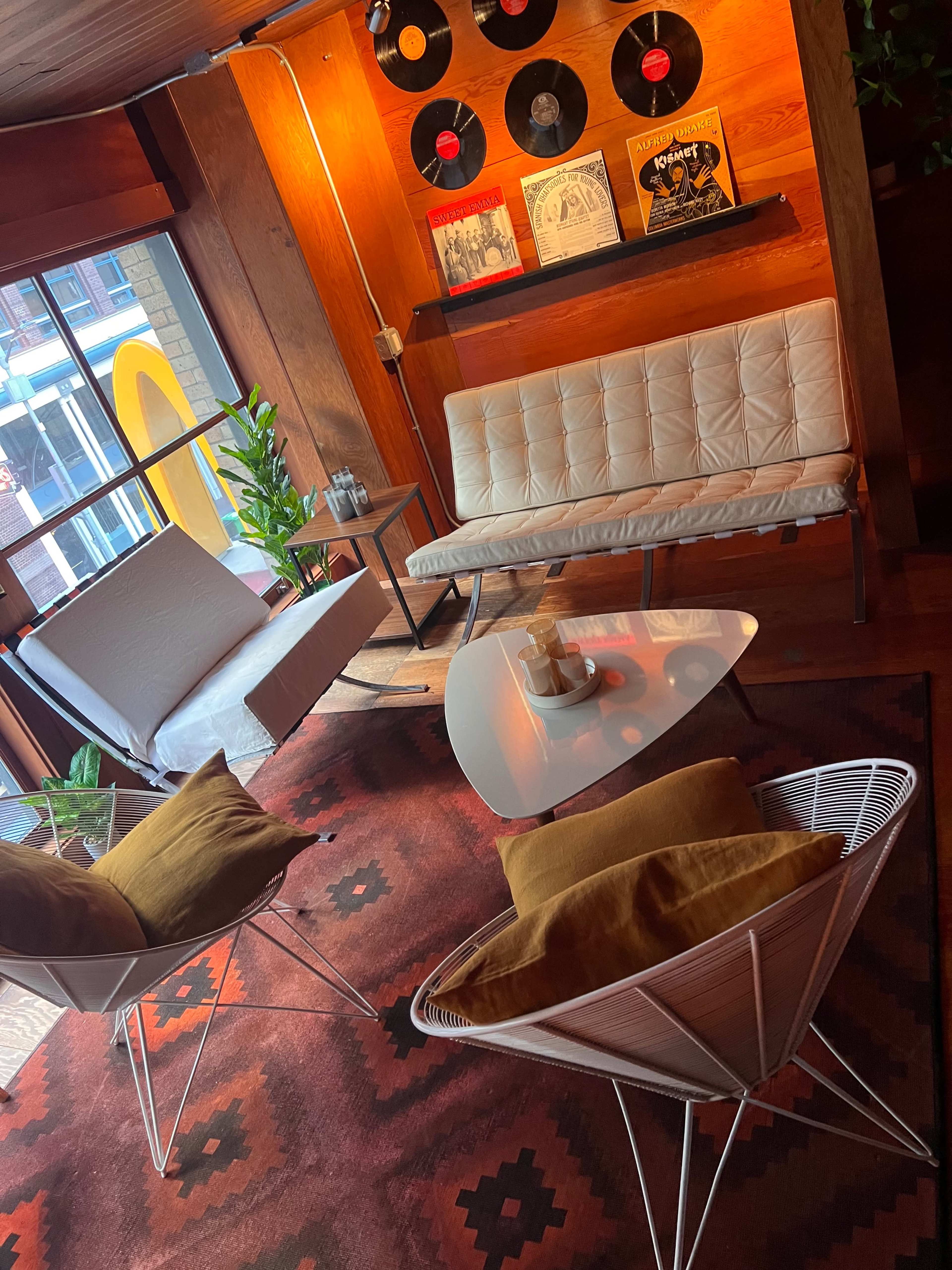 A cozy seating area with a white modern sofa, two lounge chairs, and a coffee table, set against a backdrop of wooden walls and vintage vinyl records.