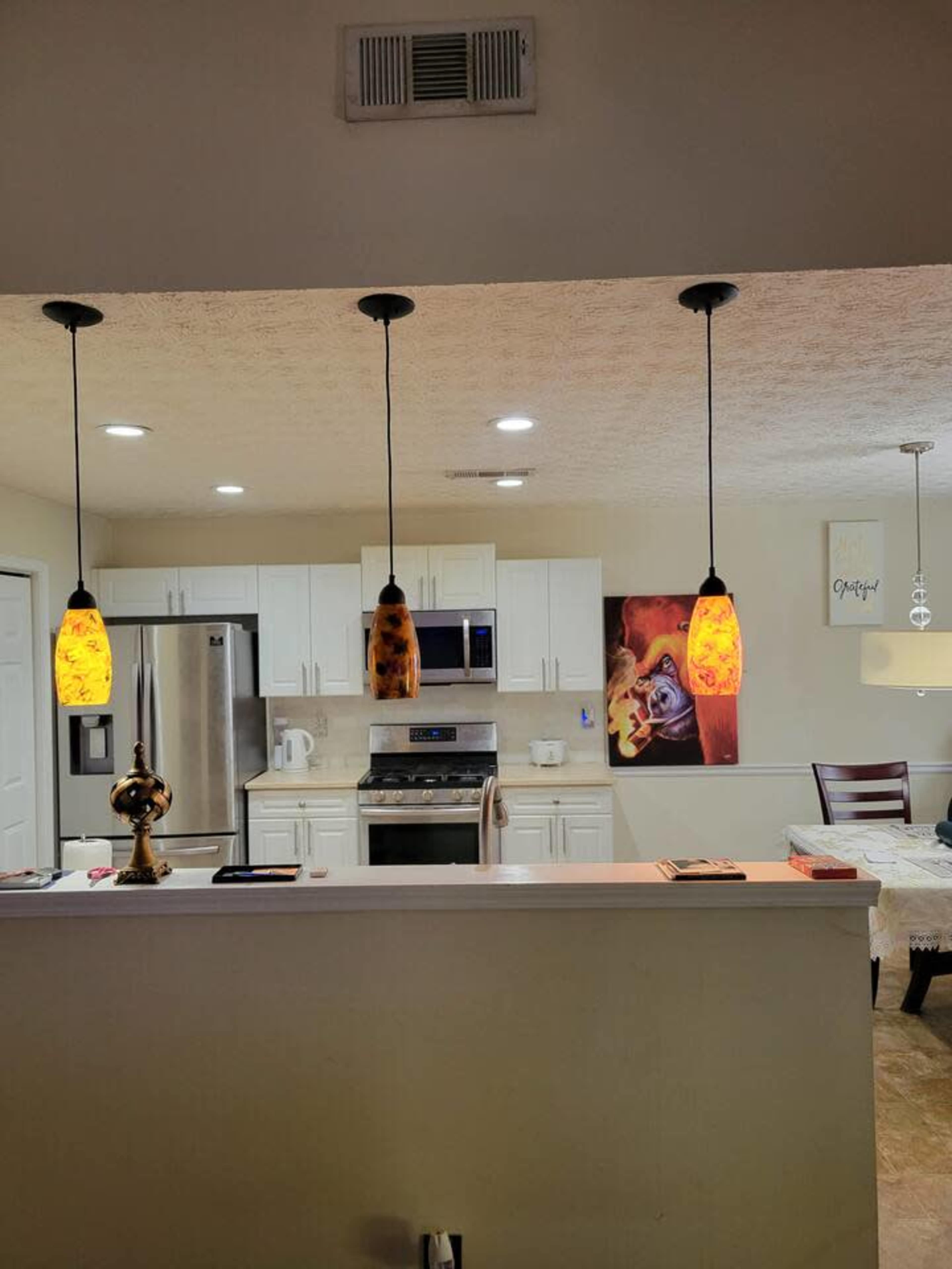 The image shows a modern kitchen with white cabinets, stainless steel appliances, and pendant lights hanging over a countertop.