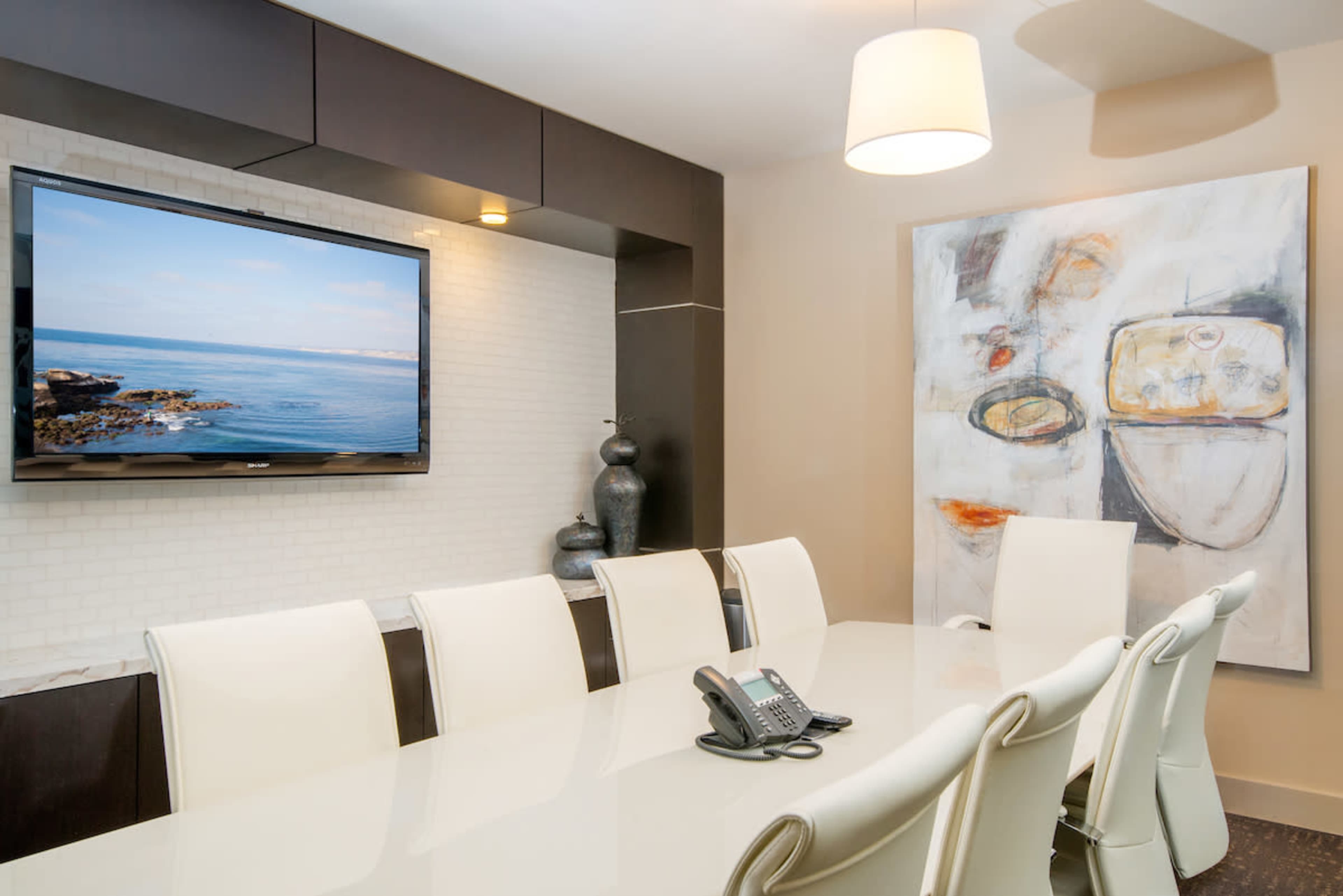A modern conference room with a large table, white chairs, a television mounted on the wall, and an abstract painting beside it.