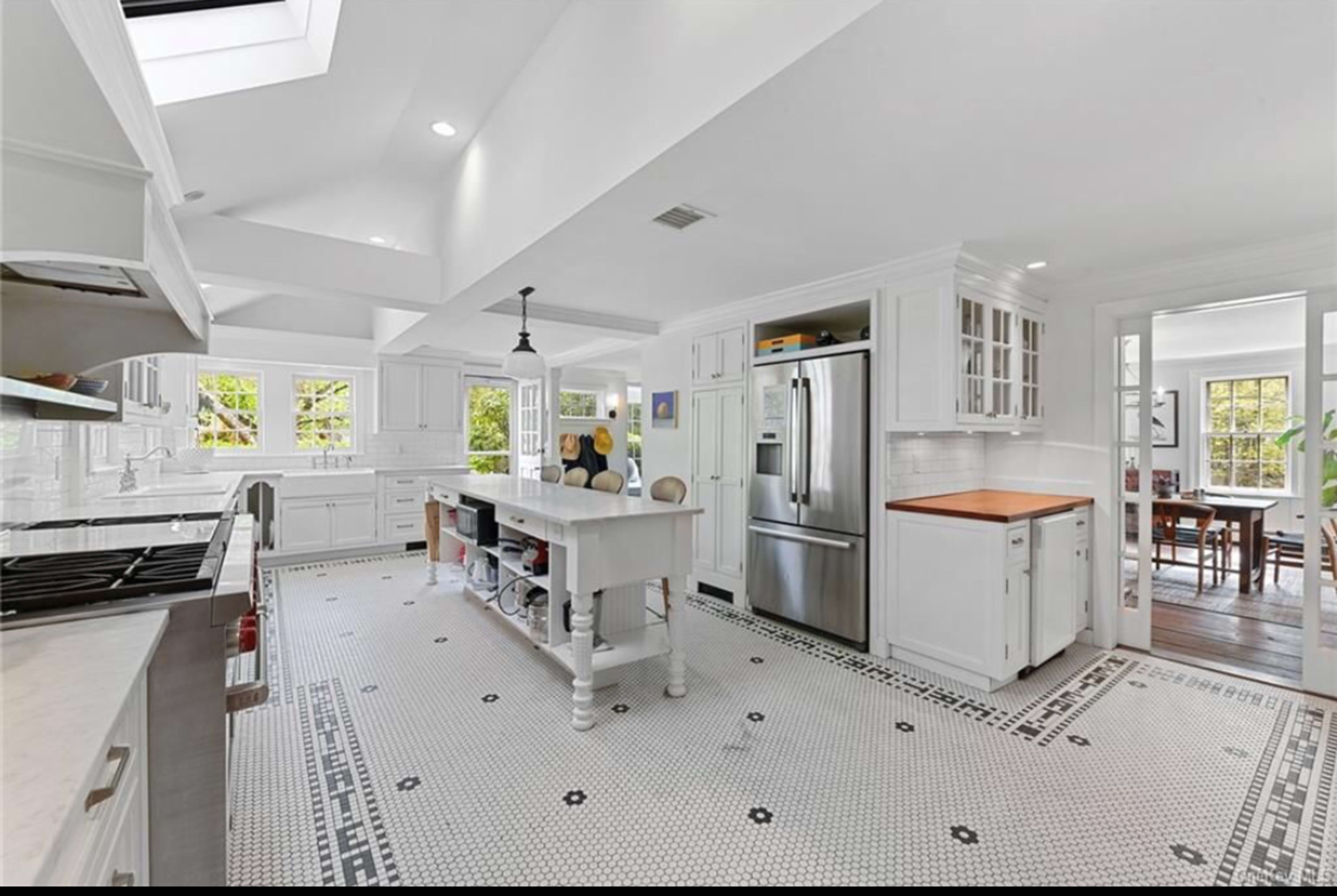 The image shows a bright, modern kitchen with white cabinetry, a central island, and a tiled floor featuring a black and white geometric pattern.