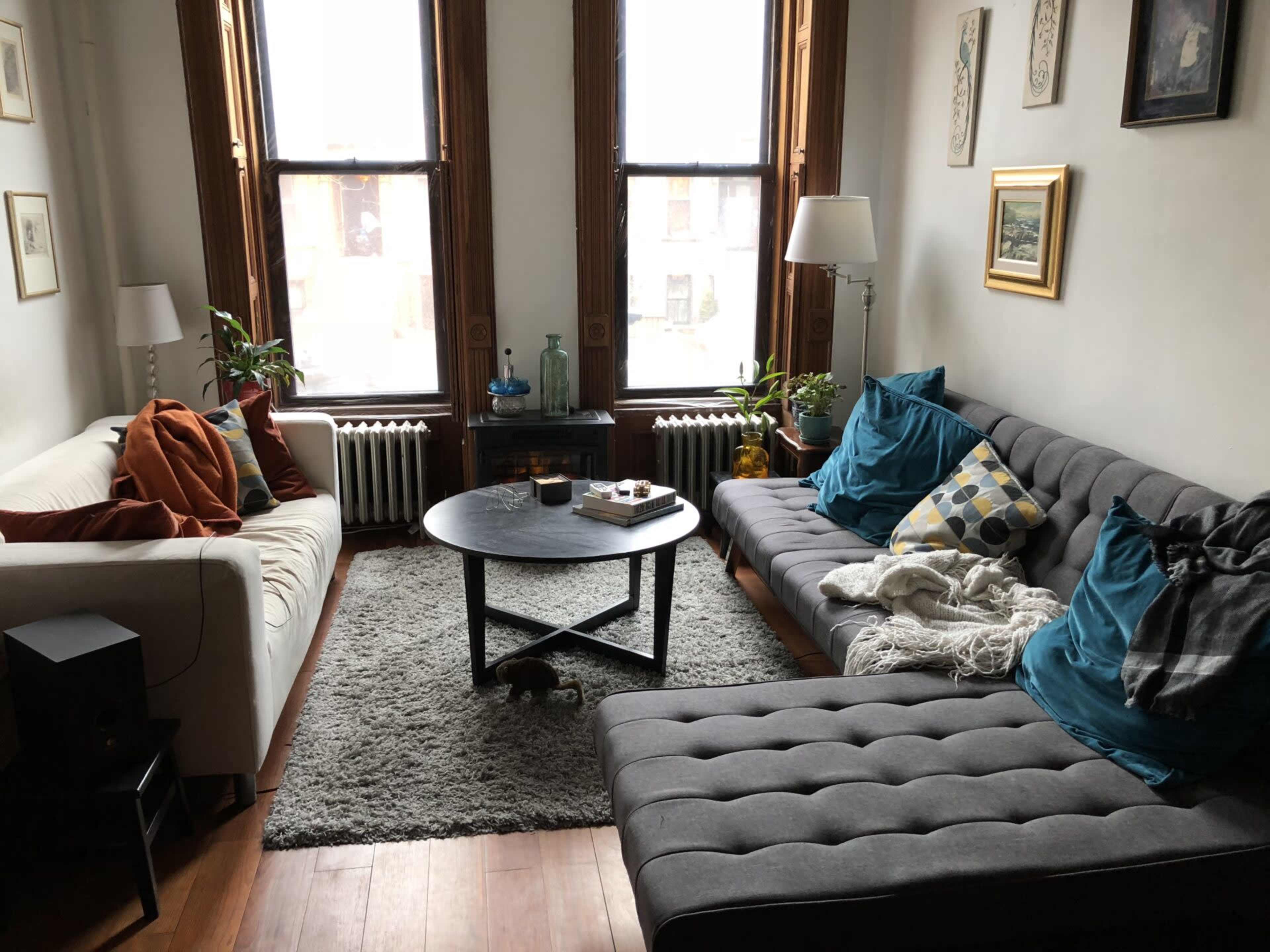 A cozy living room features two sofas, a round coffee table, and large windows with natural light illuminating the space.