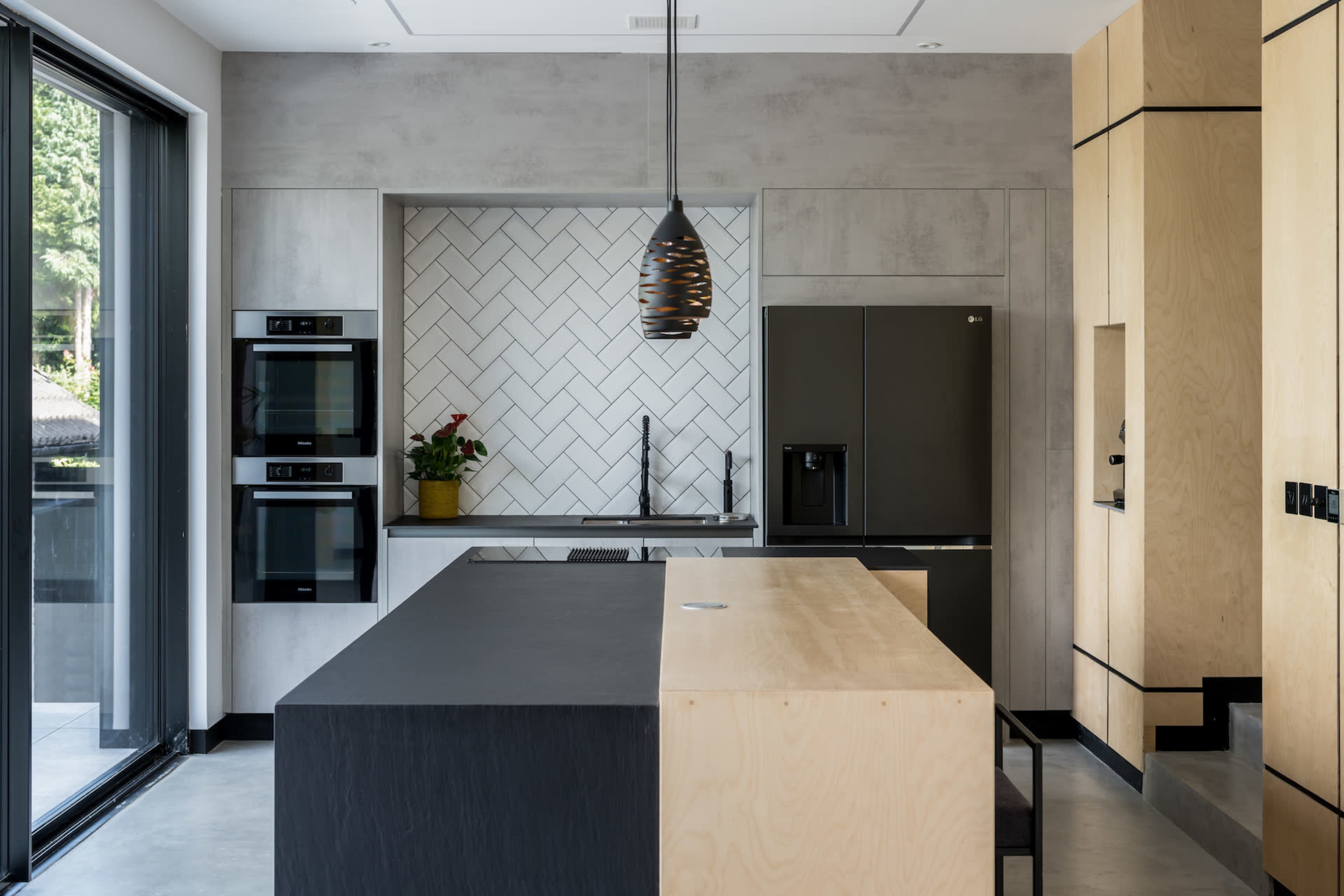 A modern kitchen featuring a large island with a black countertop, built-in appliances, and a geometric tile backsplash.