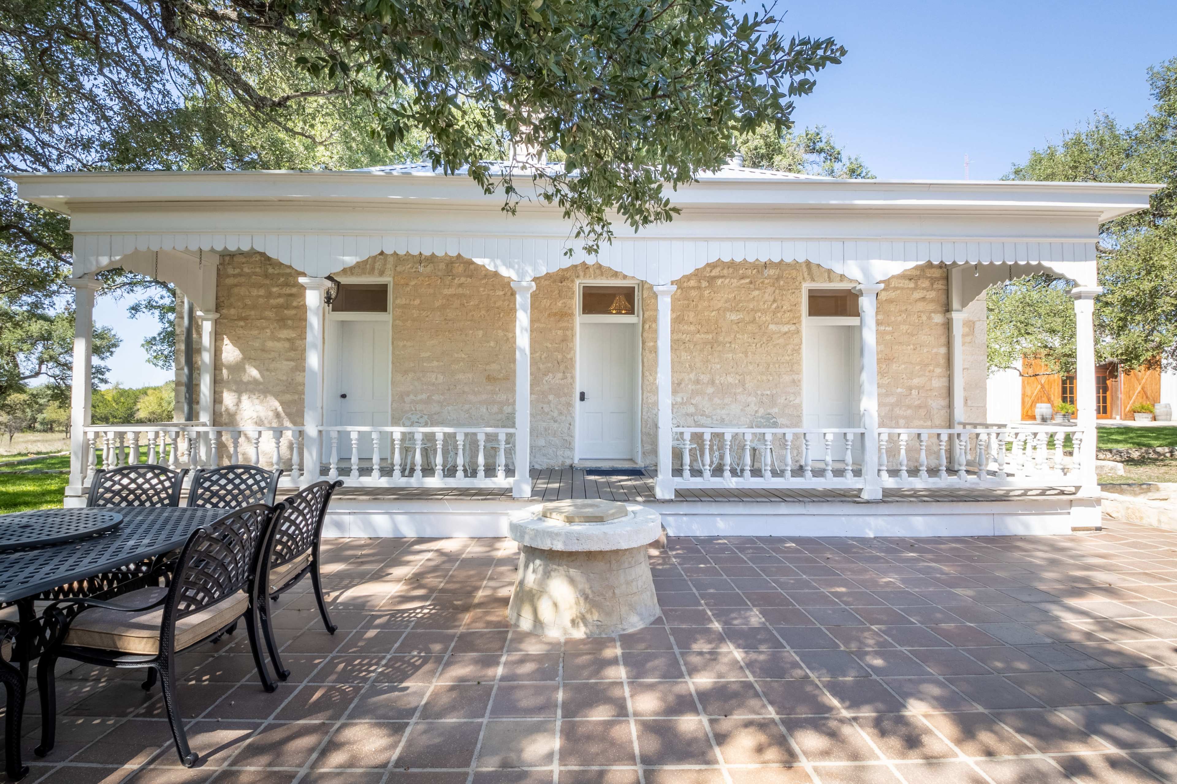 The image shows a stone house with a white porch and a patio area featuring a seating arrangement and a fire pit.