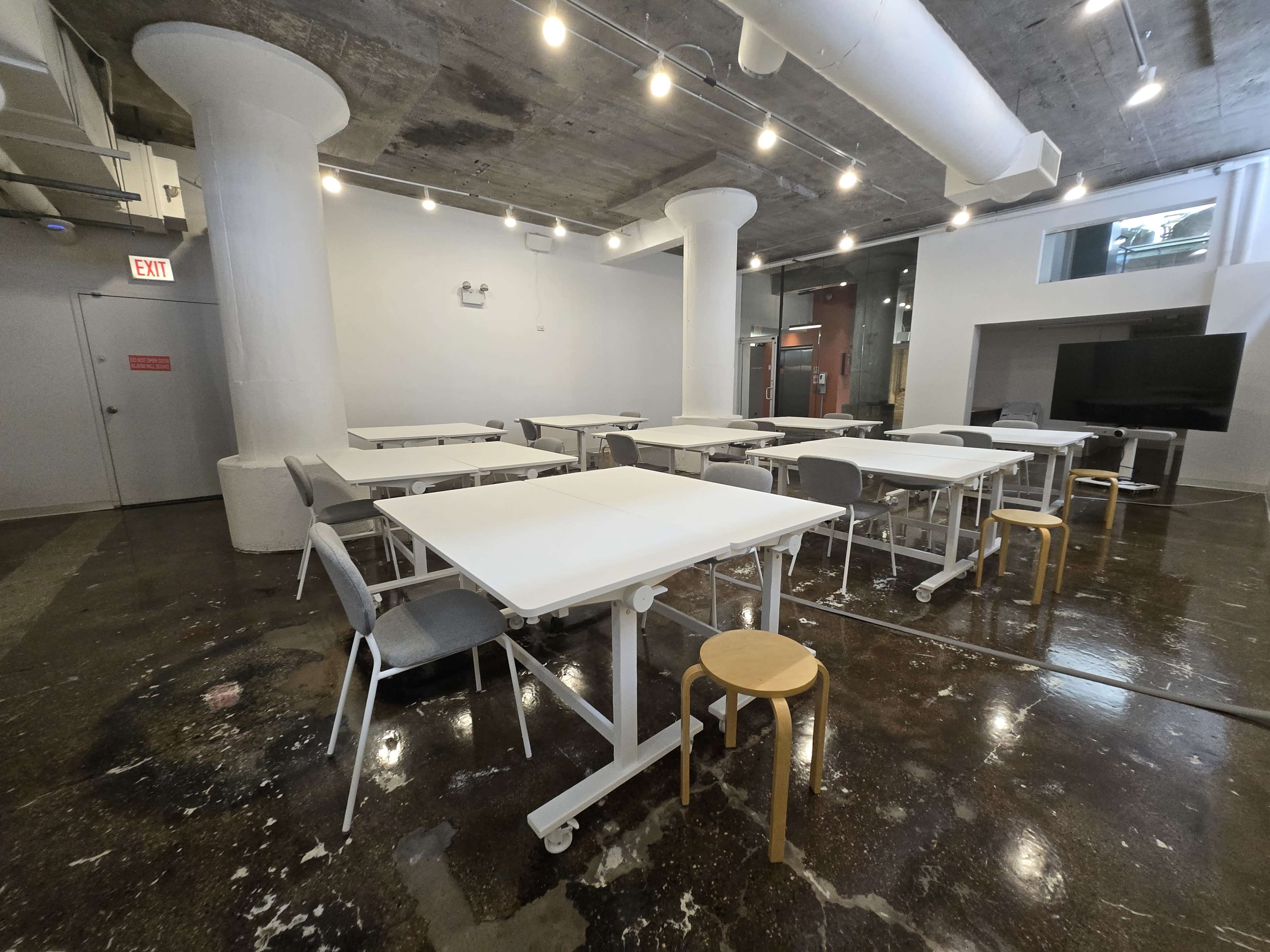 The image shows a spacious, modern classroom with several movable tables and chairs arranged in a clean, well-lit environment.