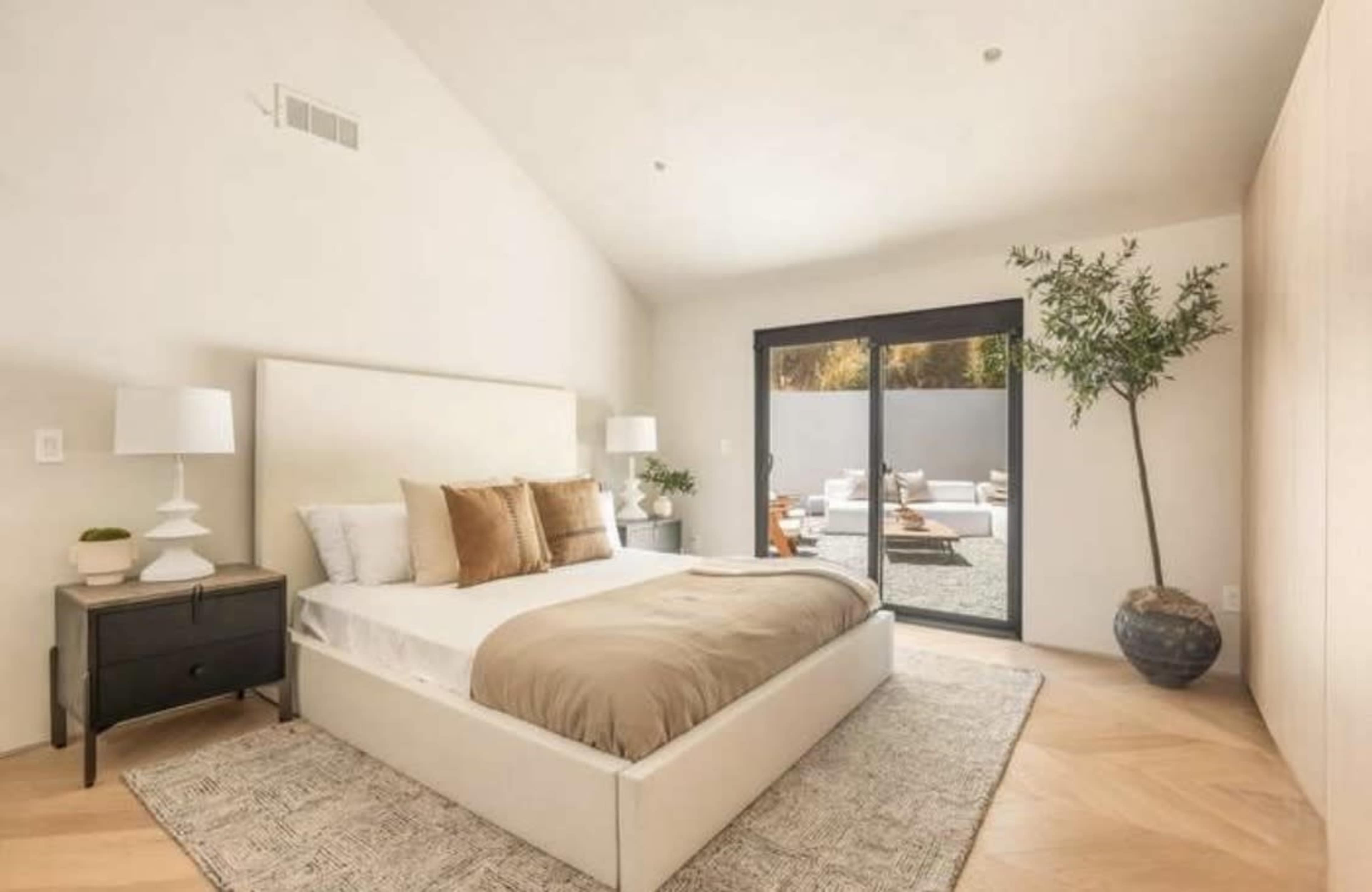 The image shows a modern bedroom with a bed, nightstands, and a large sliding glass door leading to an outdoor area.