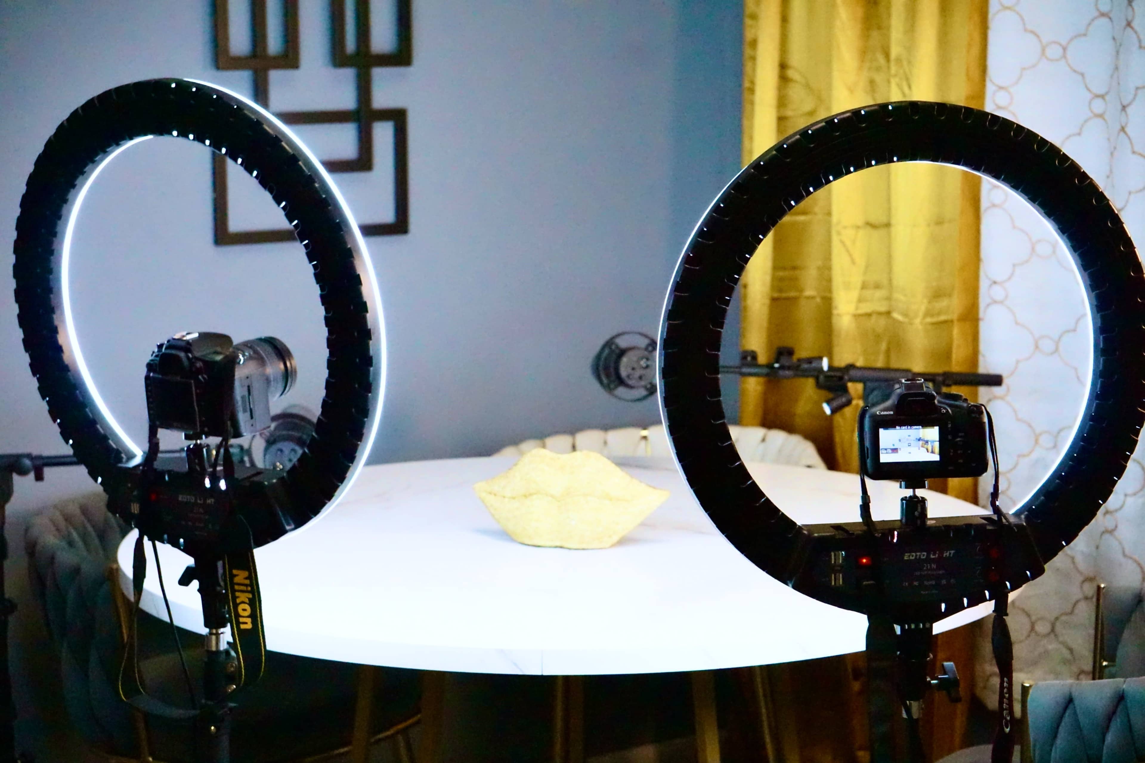 The image shows a photography setup featuring two ring lights and cameras positioned on a table with a decorative bowl in the center.