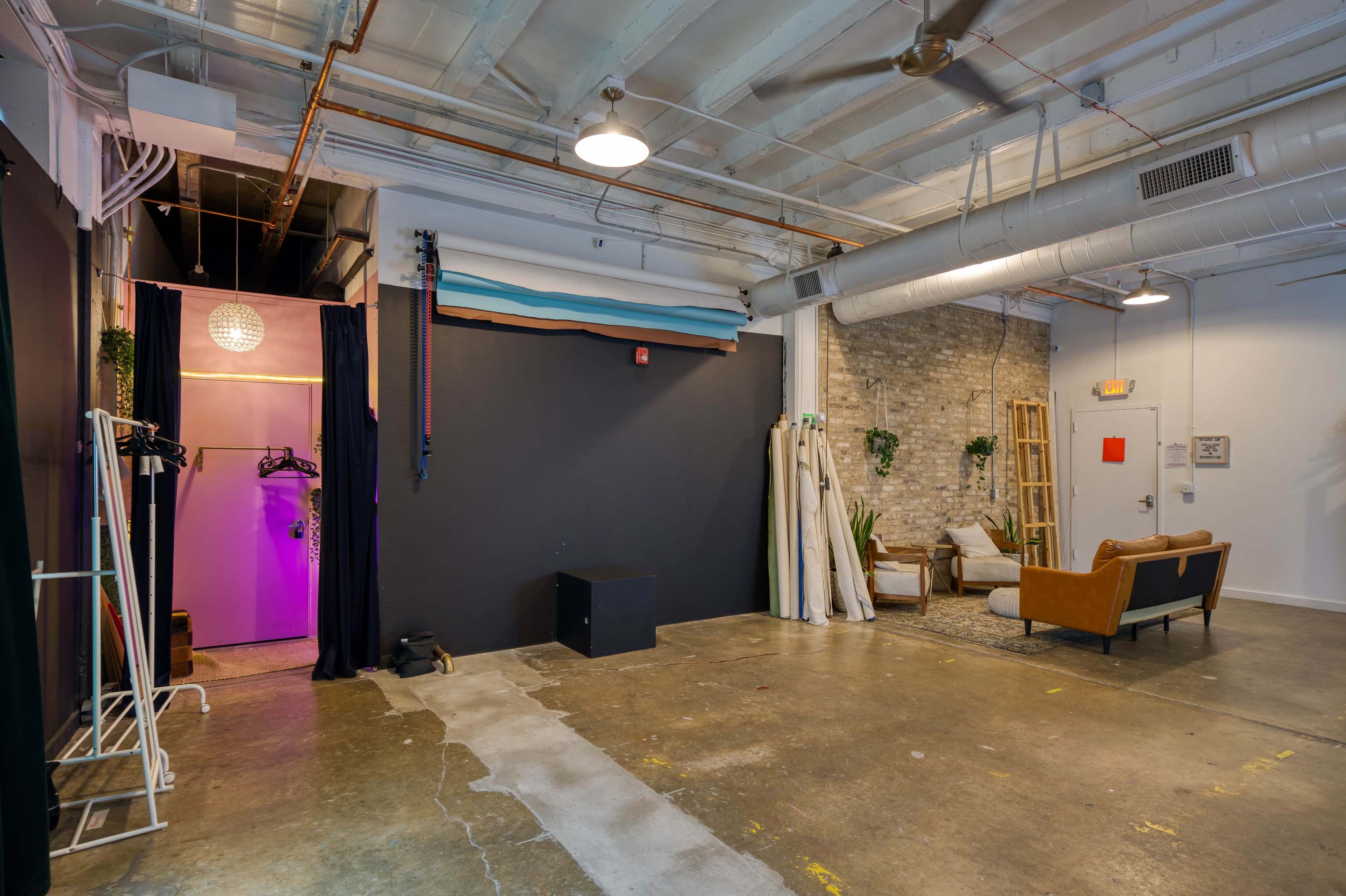 An industrial-style room with exposed brick walls, concrete flooring, a seating area with a couch, and a small dressing area with a curtain.