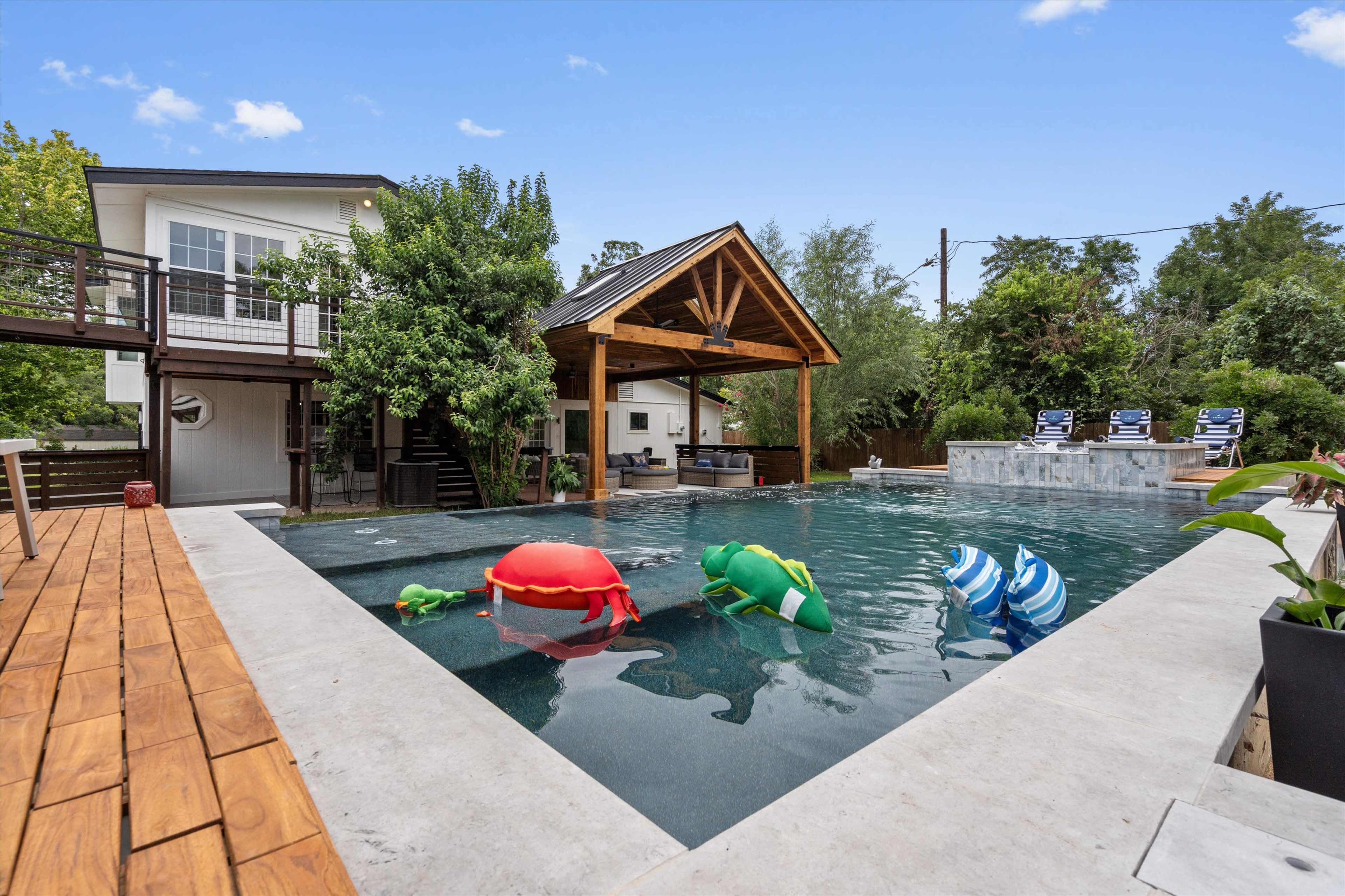 The image shows a backyard pool with colorful floats in the water, surrounded by a wooden deck and a gazebo-style structure.